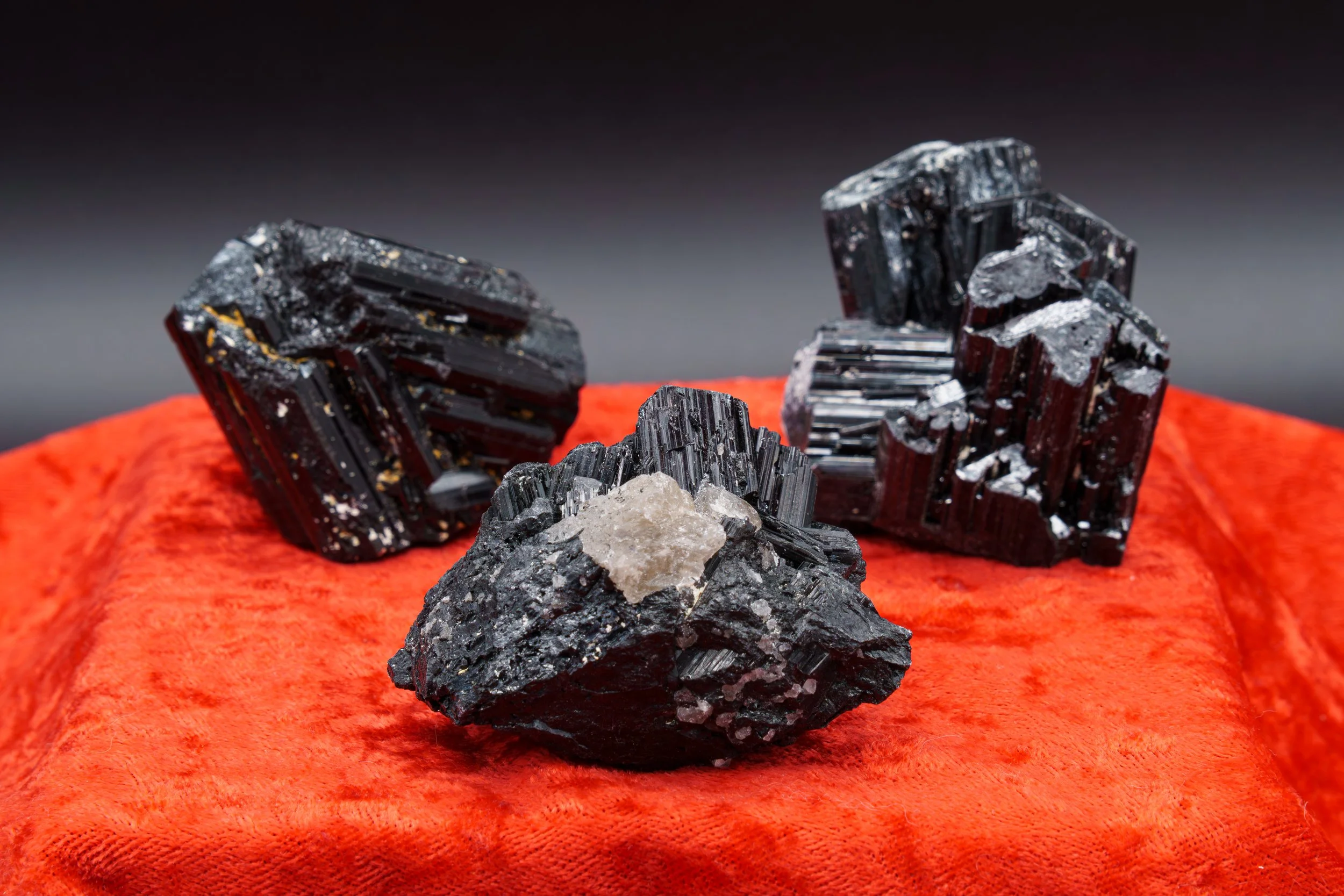Multiple black mineral crystals with a few gray crystals on top, placed on an orange fabric surface.