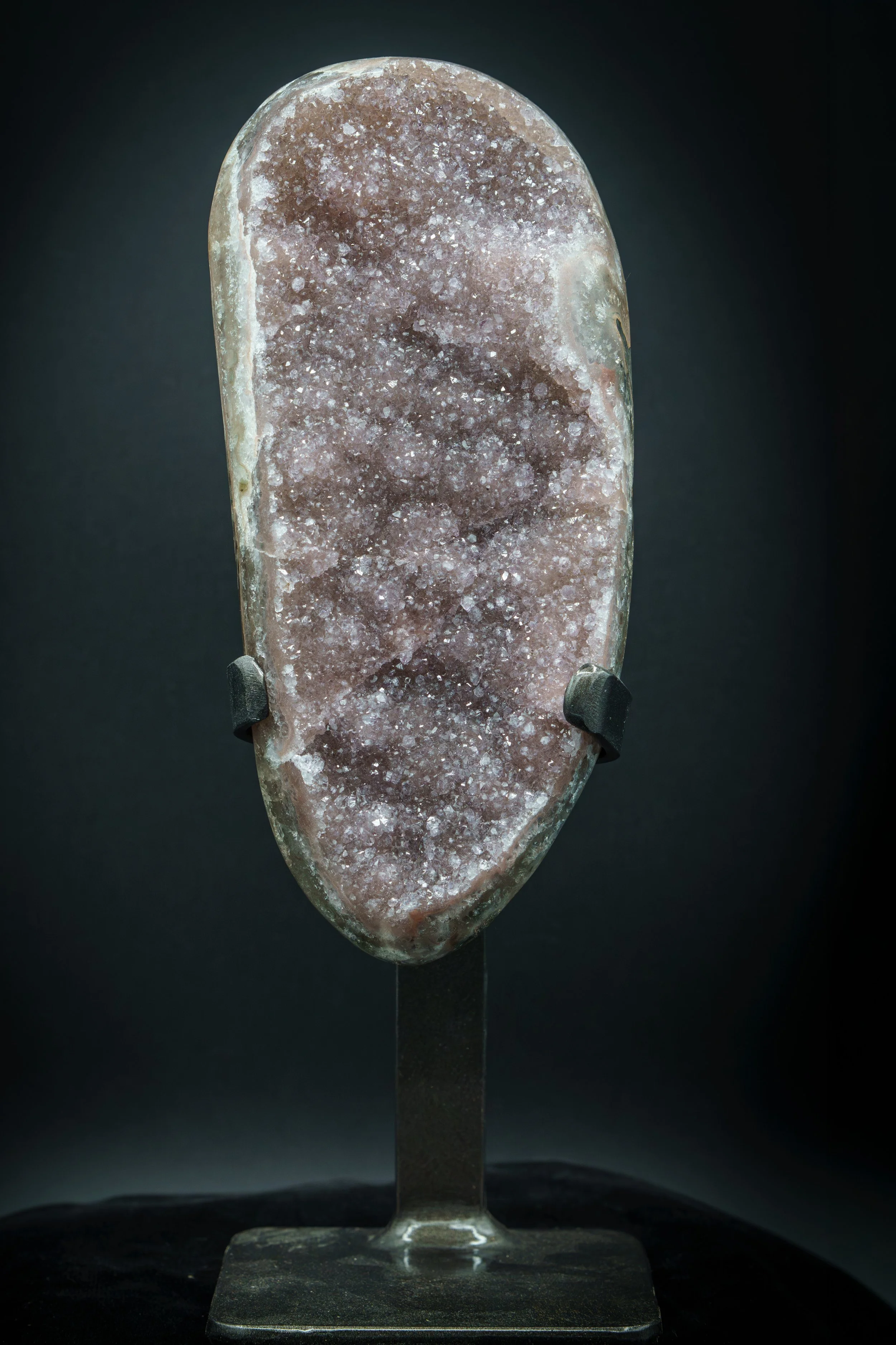 A polished pink and brown druzy gemstone carved into an ear-shaped pendant, mounted on a stand.