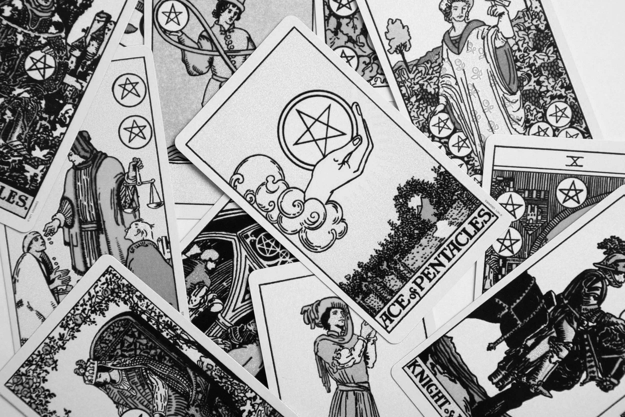 A collection of black and white tarot cards, featuring various illustrations including a hand holding a pentacle, a woman in traditional attire, a knight, and other symbolic images.