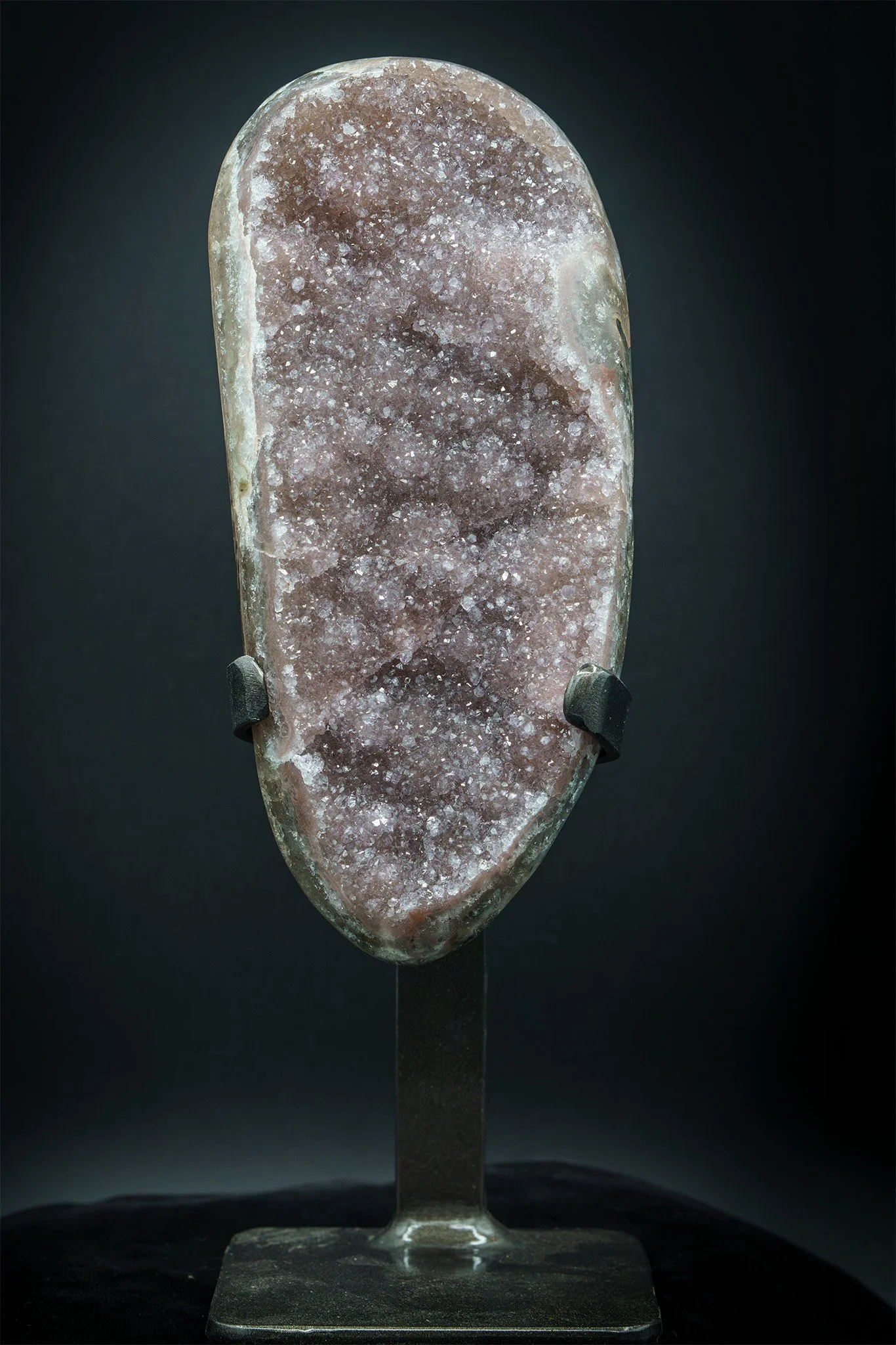 A rough, pinkish-purple geode with crystalline interior mounted in a metal stand