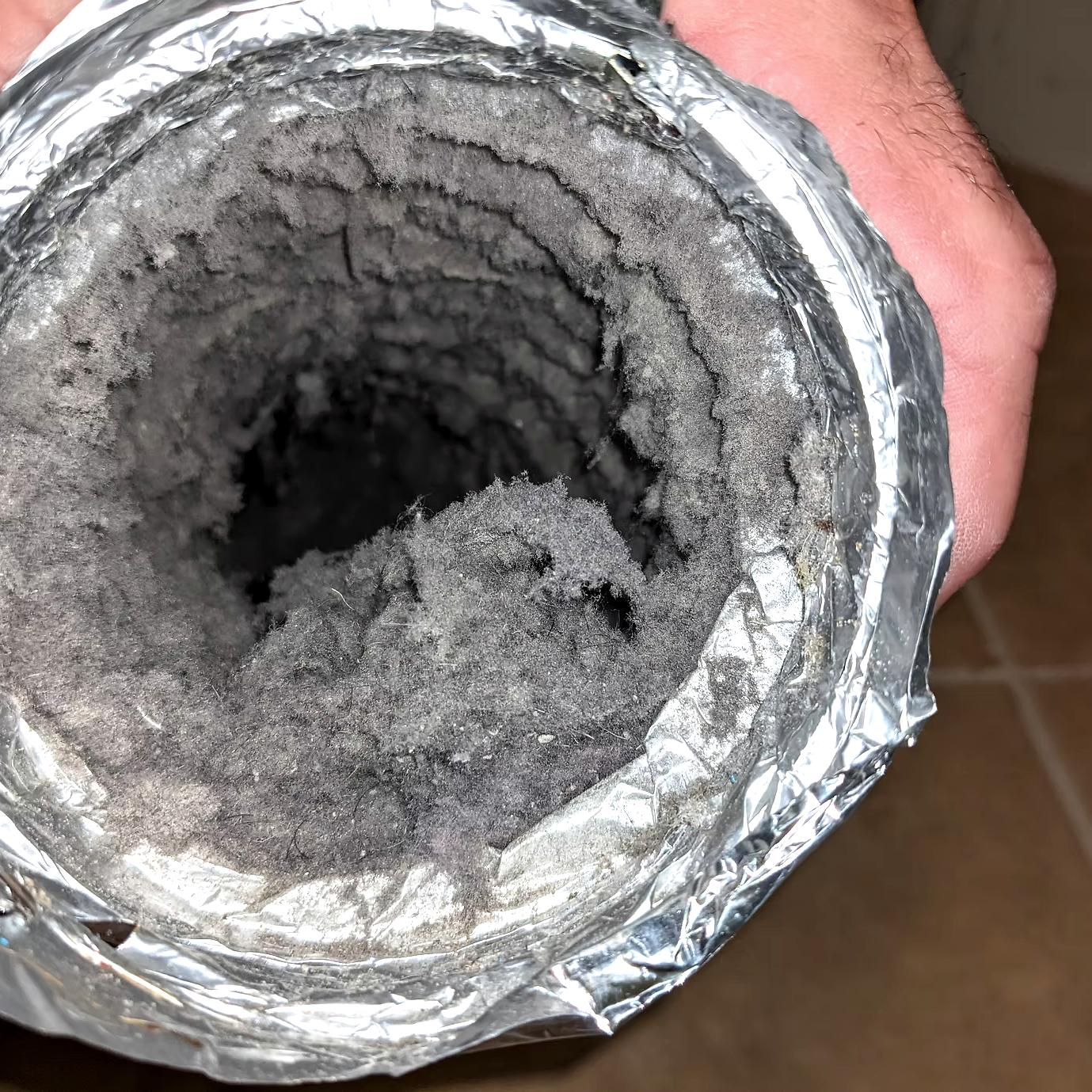 Top view of a cylindrical container filled with a black, dusty powder, covered with crinkled aluminum foil.