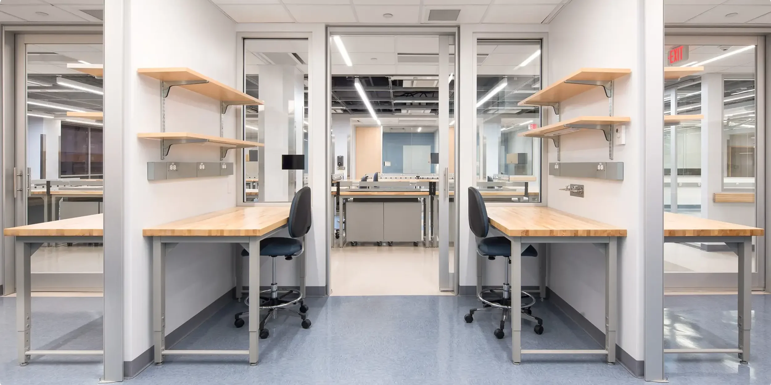 Empty workspace with desks, chairs, shelves, and glass walls in a modern office or lab.