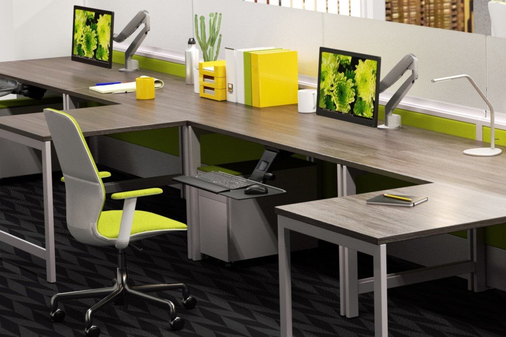 Modern office workspace with grey desks, yellow and grey chairs, dual computer monitors, green desk accessories, and a black patterned carpet.