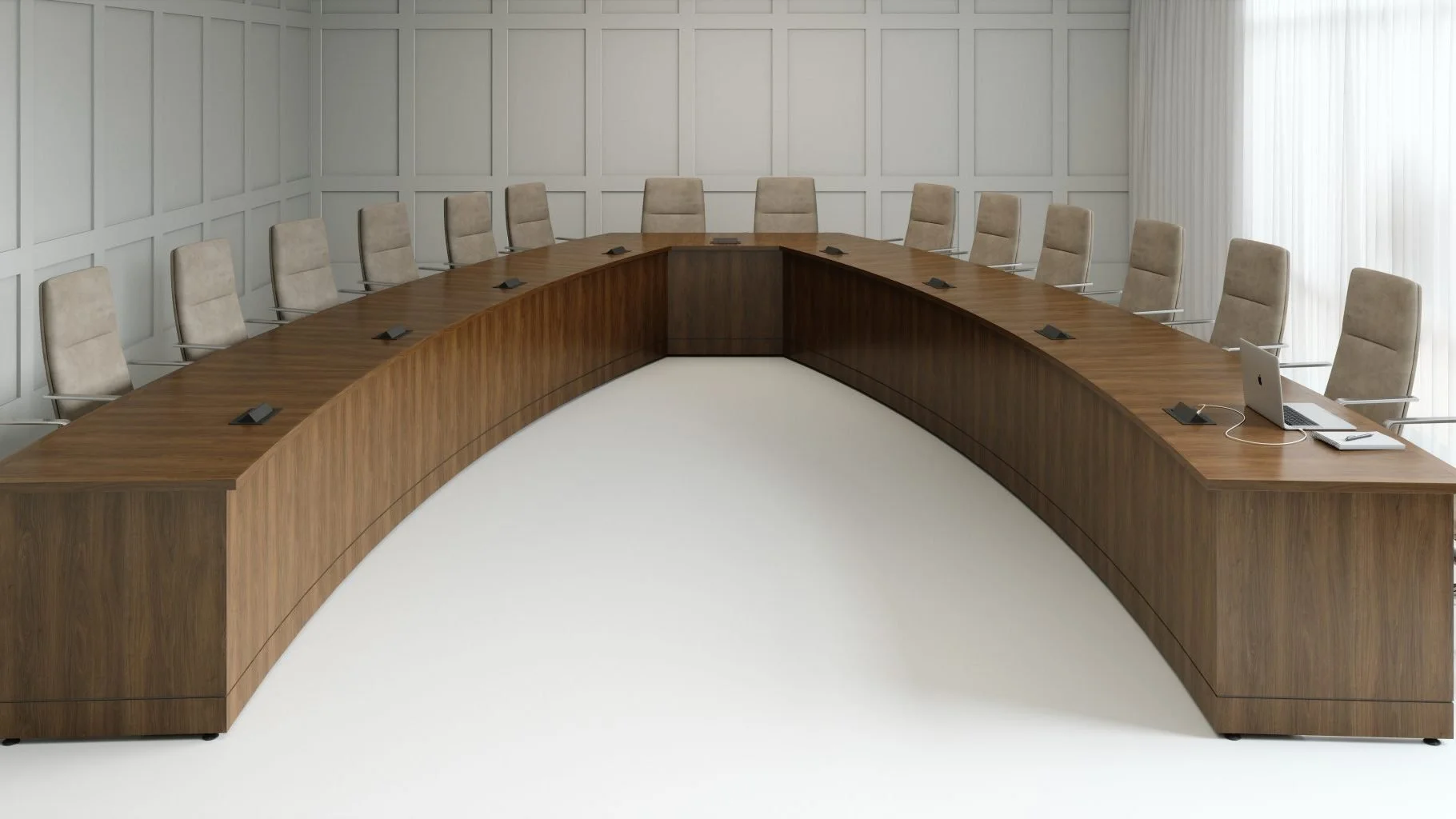 Empty conference room with a large U-shaped wooden table, beige ergonomic chairs, a laptop, notebook, and pen on the table; white paneled walls and a window with sheer curtains.