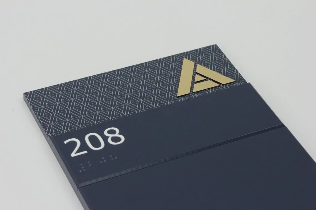 A hotel room sign displaying the number 208, Braille, and an ADA symbol with a gold triangle and arrow logo on a black background.