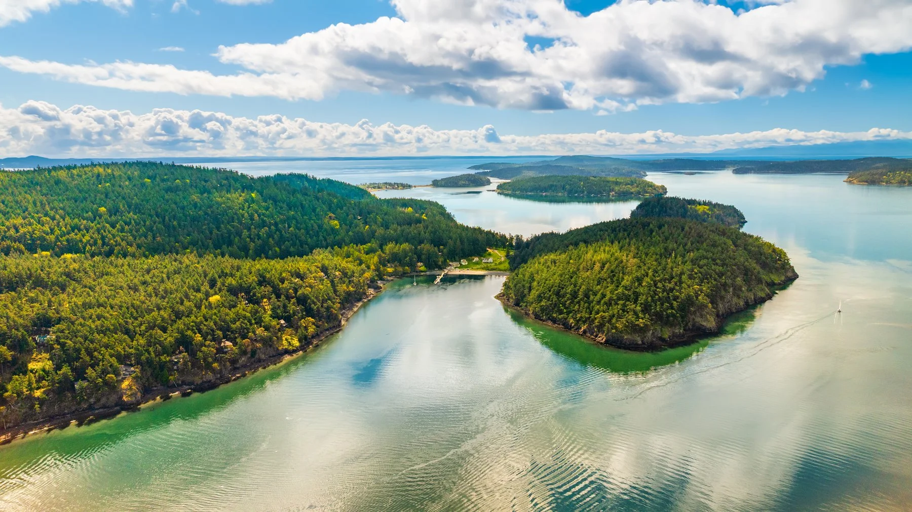Aerial view of a large body of water with green forested islands and peninsulas, under a partly cloudy sky.