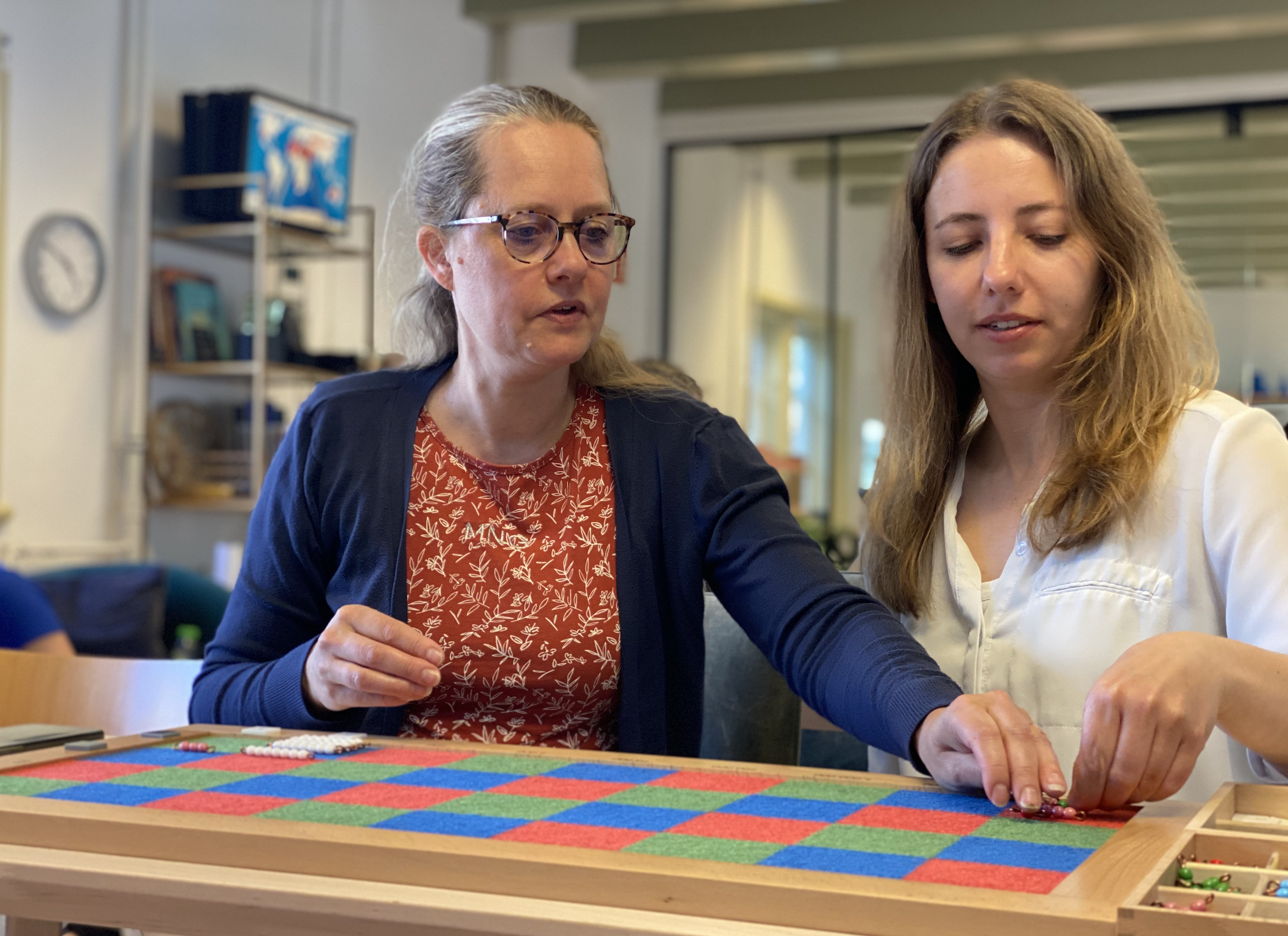 Two women practicing with Montessori material on the AMI 6-12 Diploma course in Delft at the International Montessori Institute (IMI).