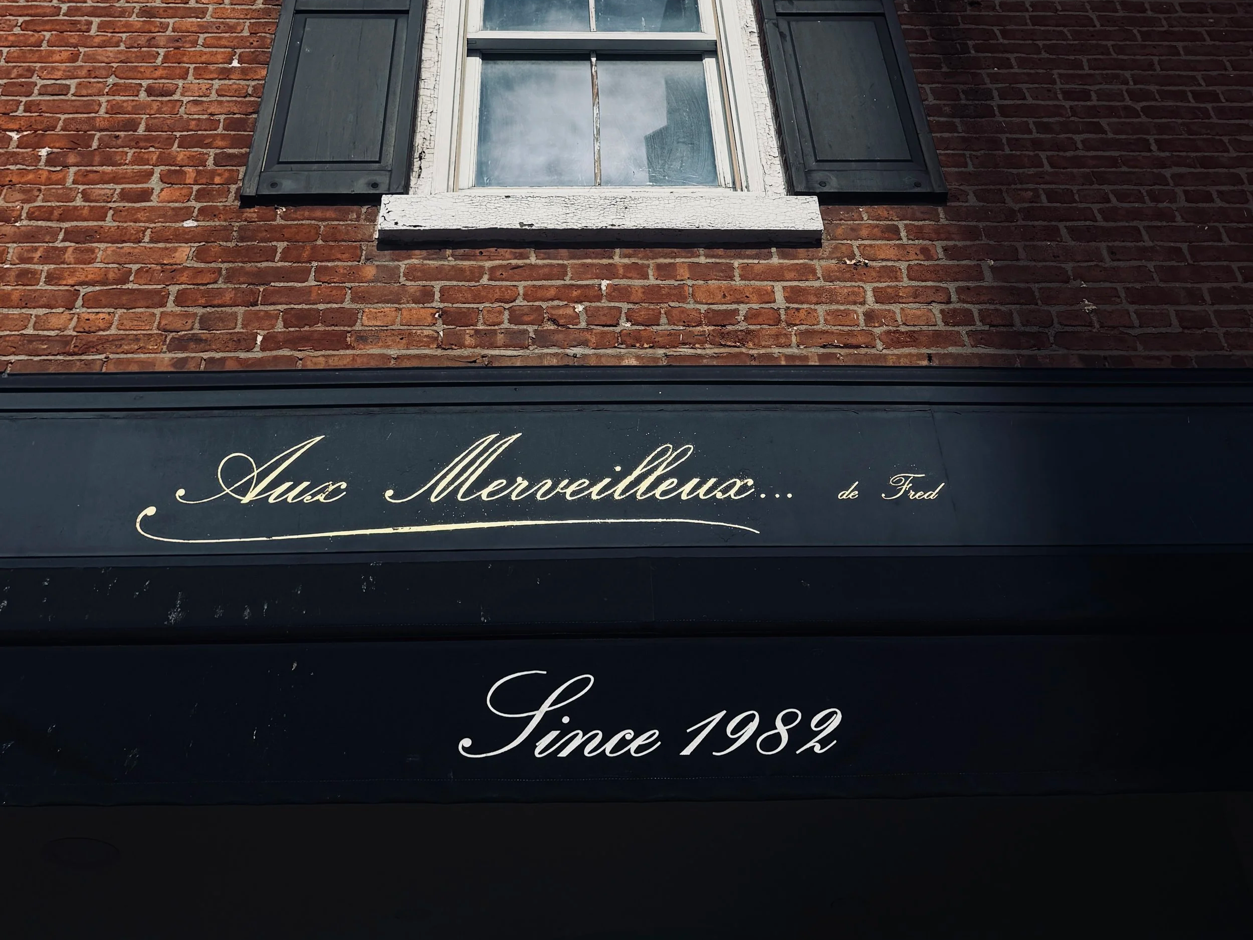 Aux Merveilleux de Fred shop sign in white script on a dark fascia, "Since 1982", French patisserie in the UK