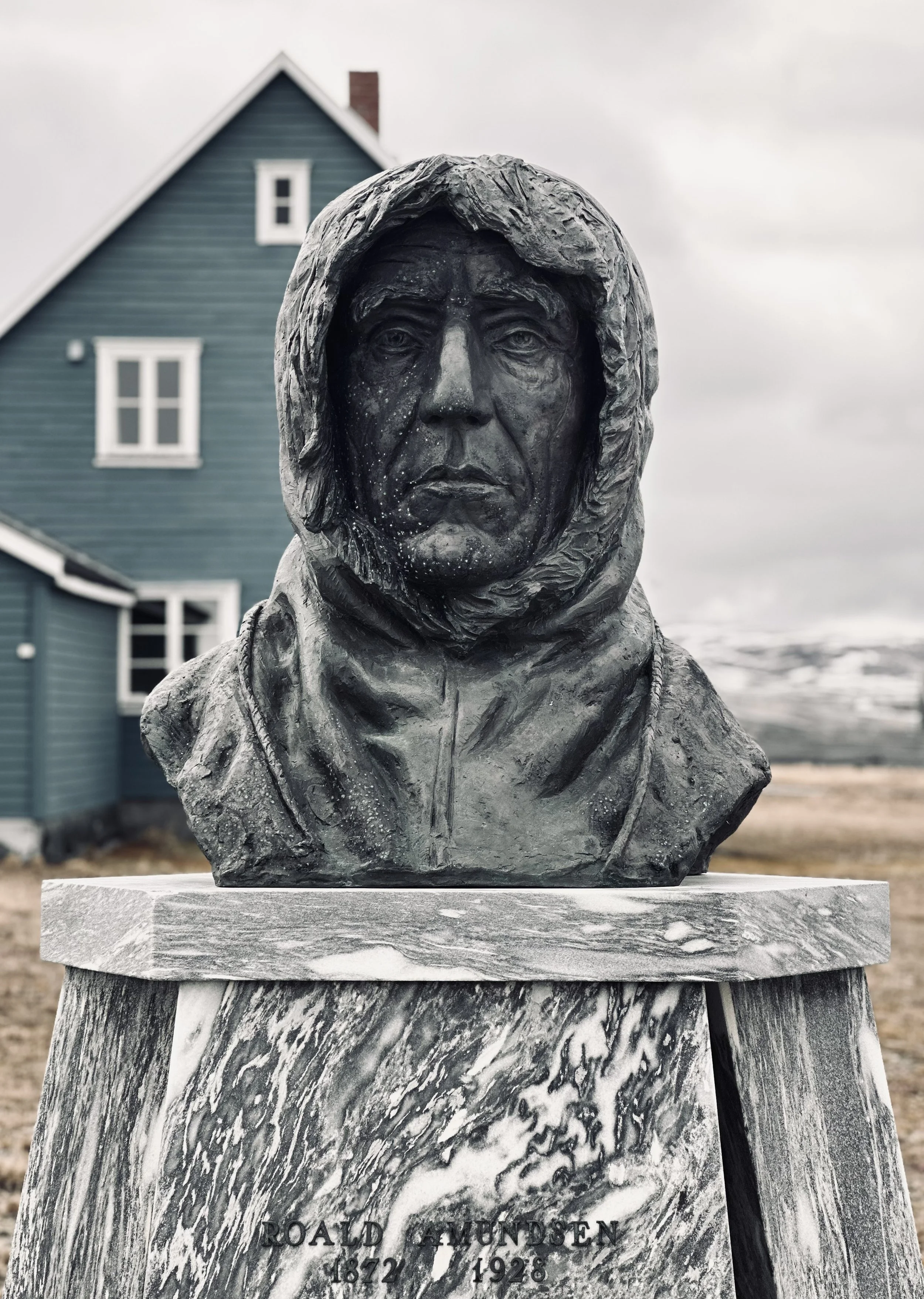 Bronze bust of Roald Amundsen, the polar explorer, with a serious expression, wearing a hooded coat. The bust is mounted on a marble pedestal with his name and dates, 1872-1928.