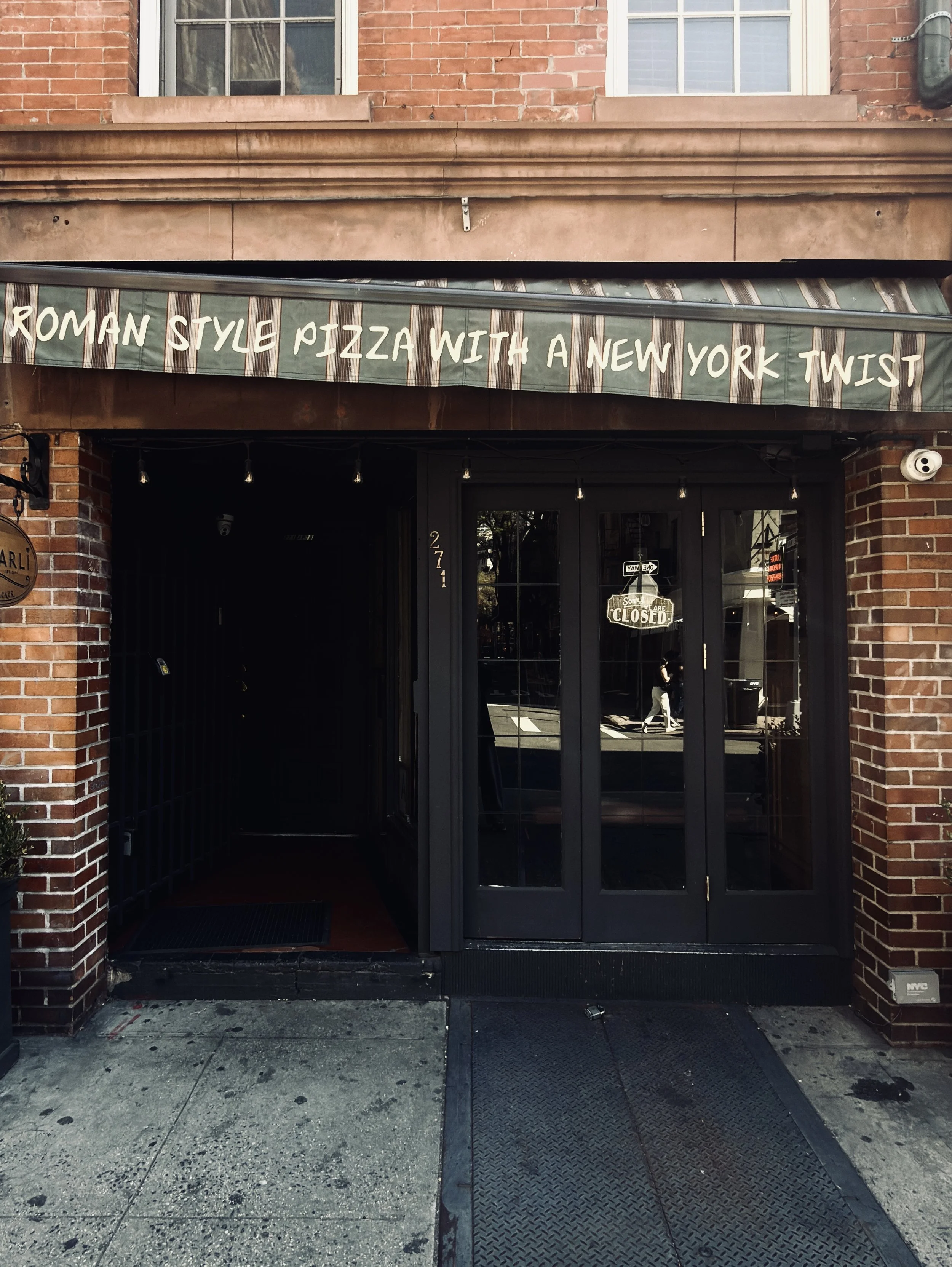 Roman style pizza with a New York twist" hand-painted on a green fascia over a pizzeria door, New York