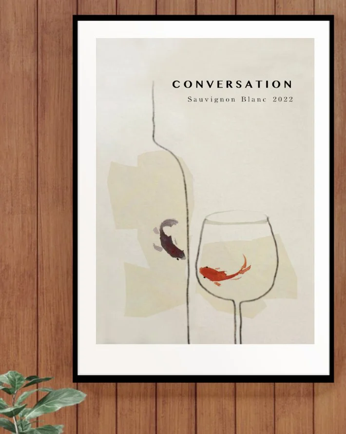 A minimalist art print featuring a wine glass with a red fish inside, and a wine bottle outline with a purple fish inside, with the text "CONVERSATION Sauvignon Blanc 2022" at the top, hanging on a wooden wall.