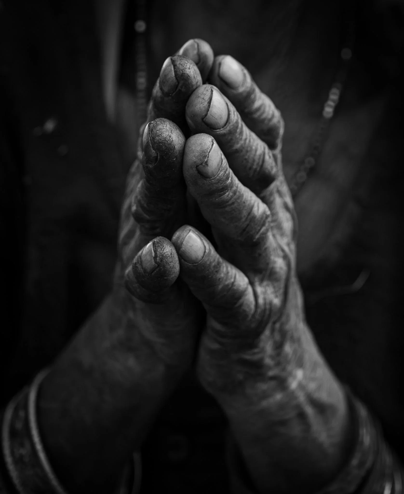 Close-up black and white photo of an old hand, emphasizing the rough skin and long fingernails, with a dark and blurred background.
