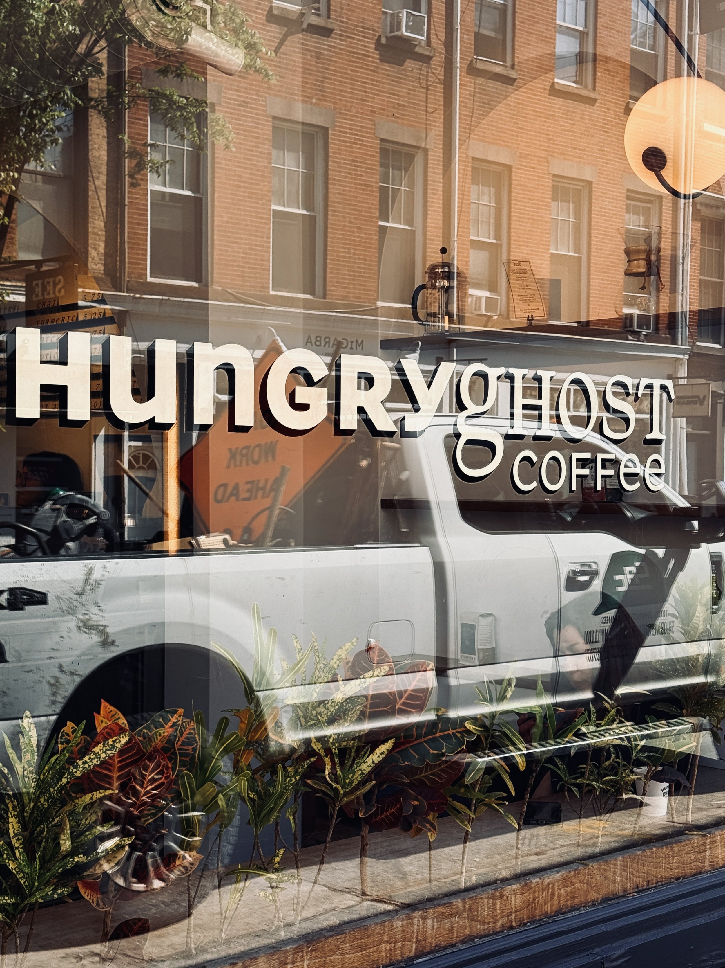 Hungry Ghost Coffee logo on a café window reflecting brick buildings, New York