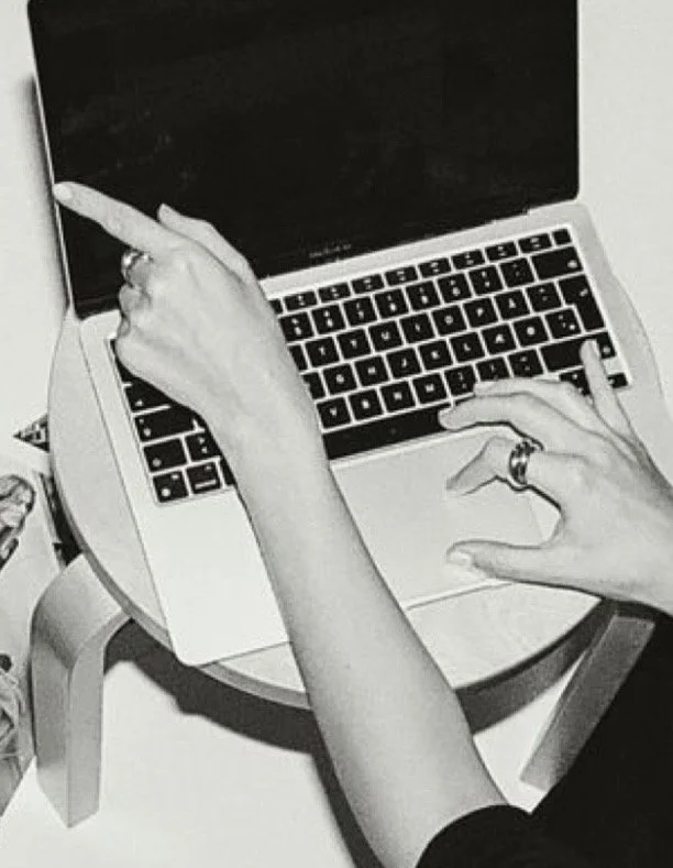 A person using a laptop computer with a black screen, pointing at the screen with their left hand and typing with their right hand, wearing rings on both hands.