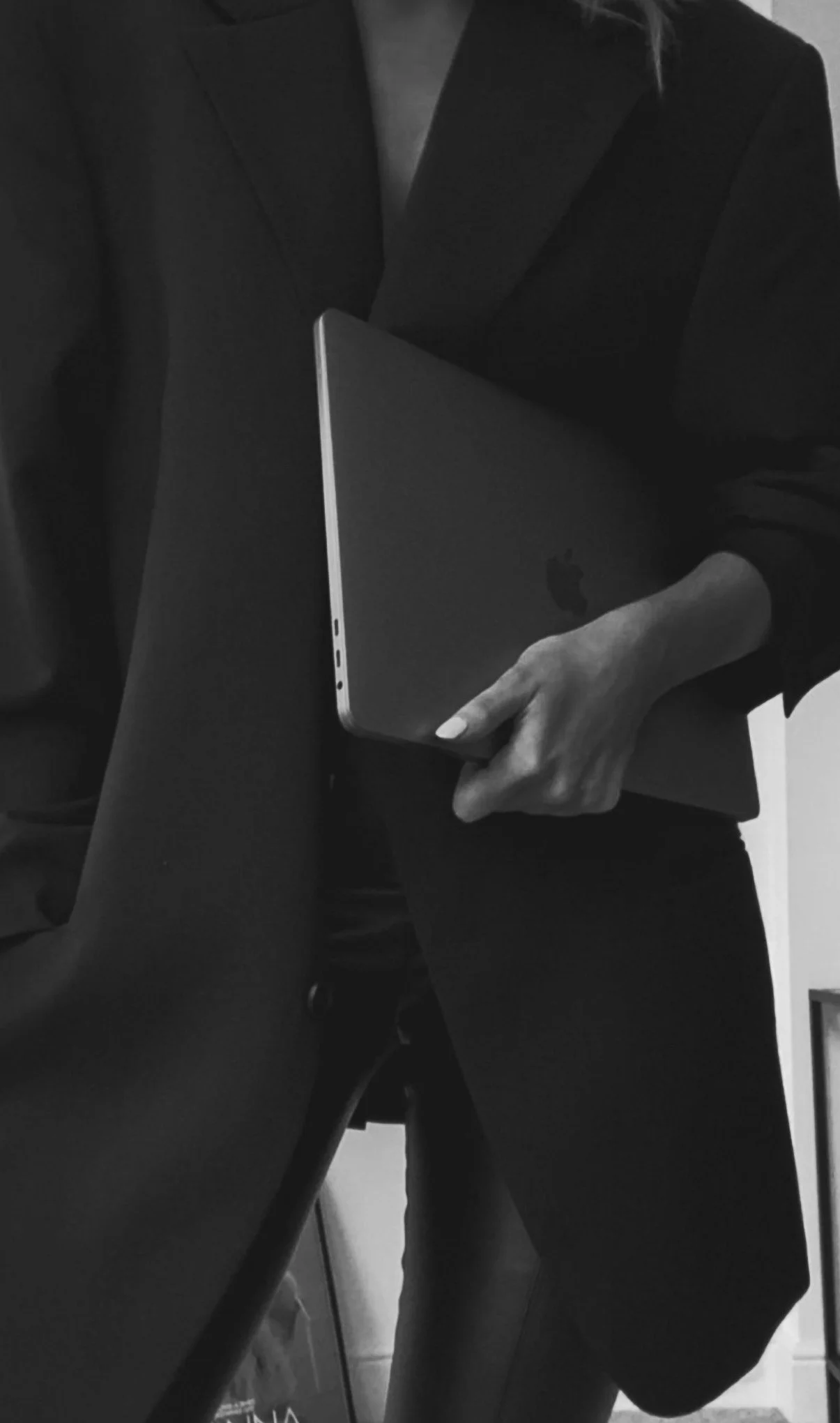 Person wearing dark clothing holding a closed MacBook laptop.