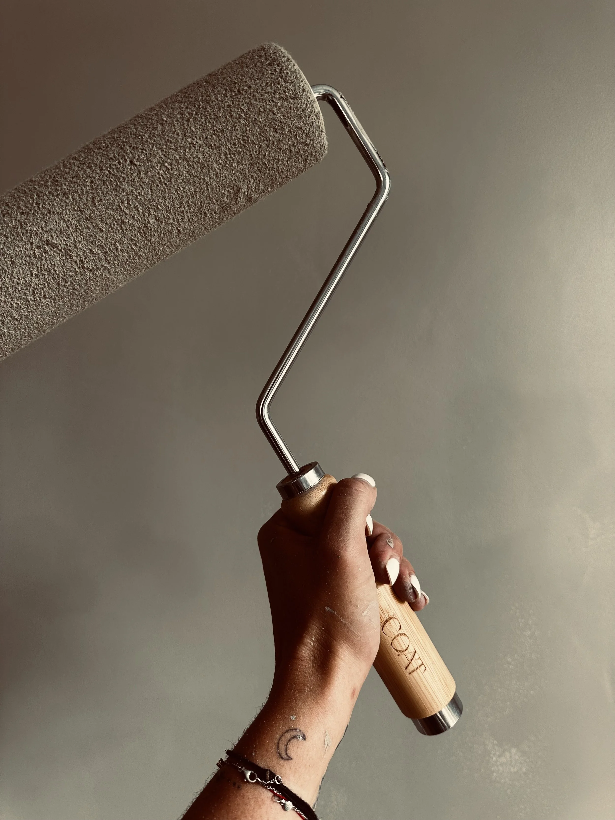 A hand holding a paint roller with a beige foam cover against a plain wall.