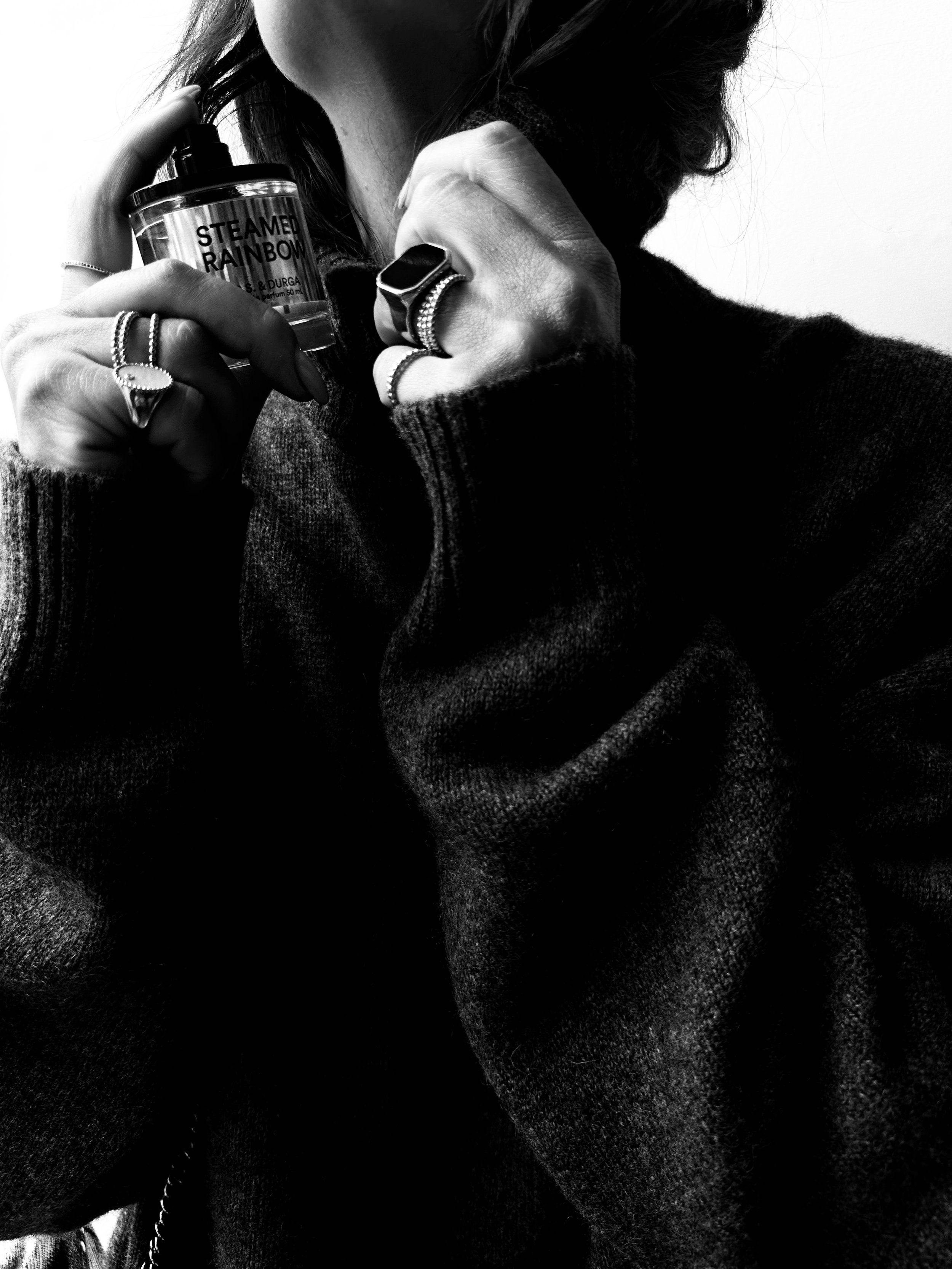 Person holding a container labeled 'Steamer Rainbow' with their face partially visible, wearing rings and a dark sweater, in black and white.
