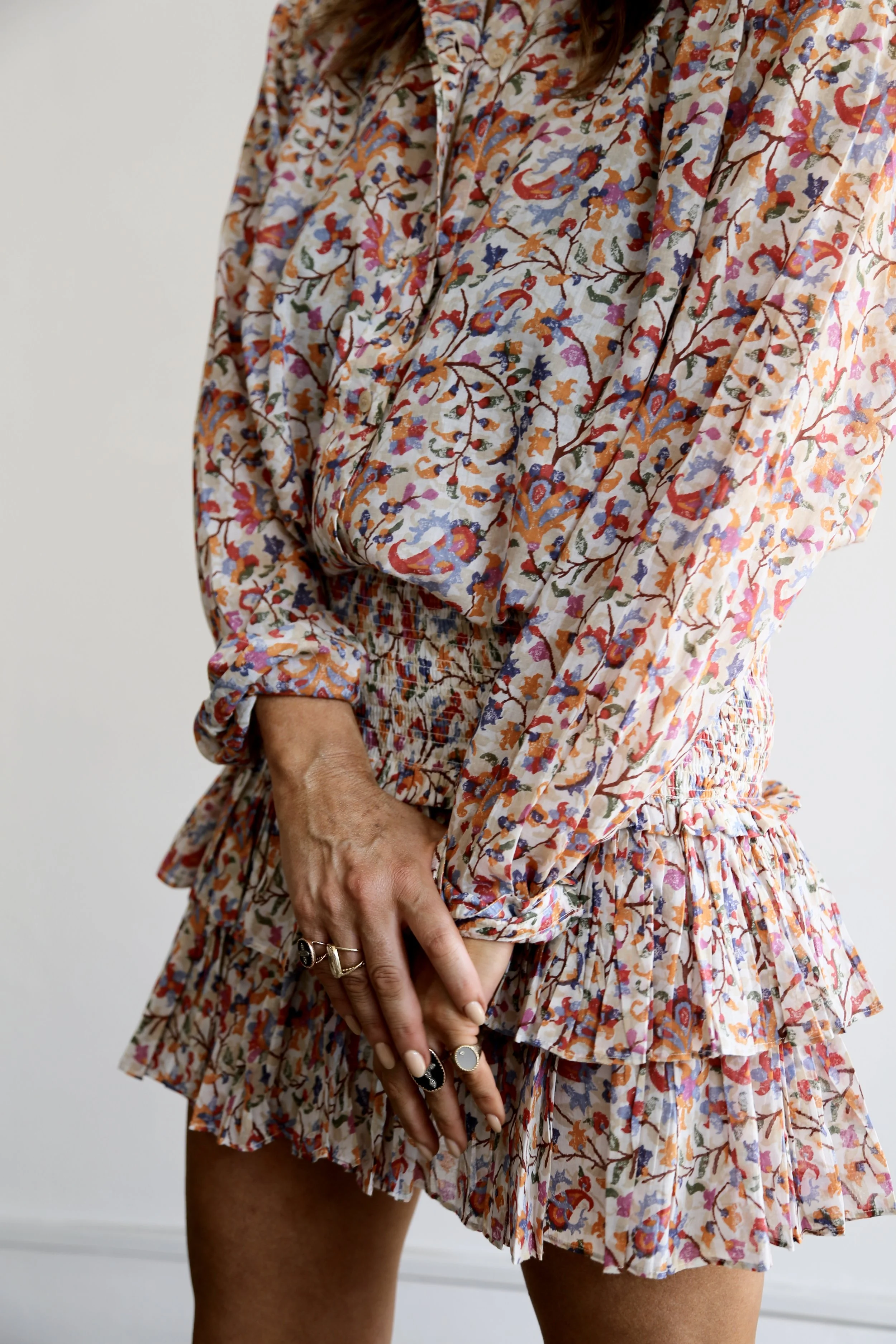Close-up of a person wearing a floral patterned dress with ruffled details, standing with hands clasped in front.