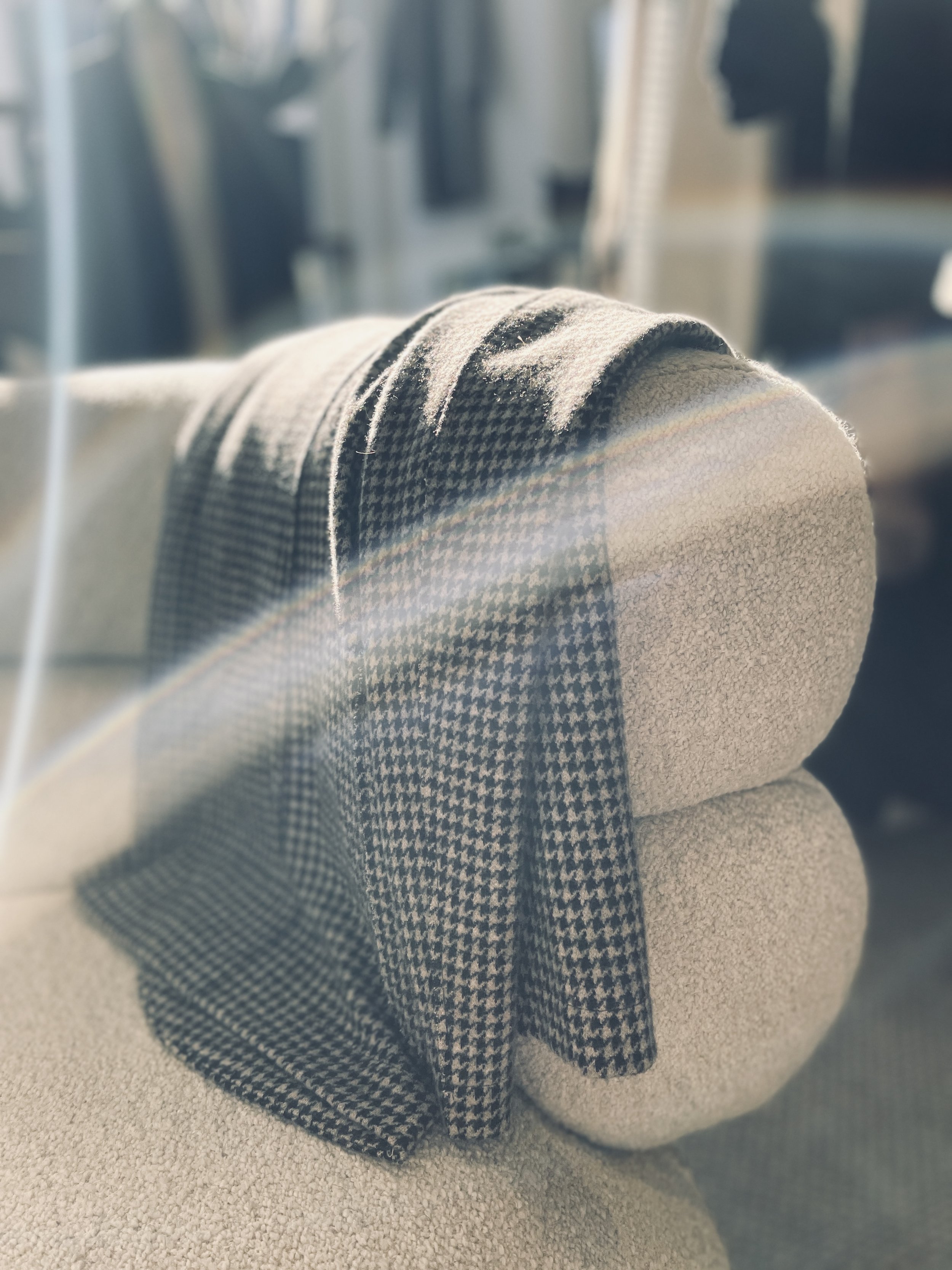 Close-up of a rolled-up houndstooth patterned scarf on the armrest of a beige fabric couch, with sunlight shining on it.