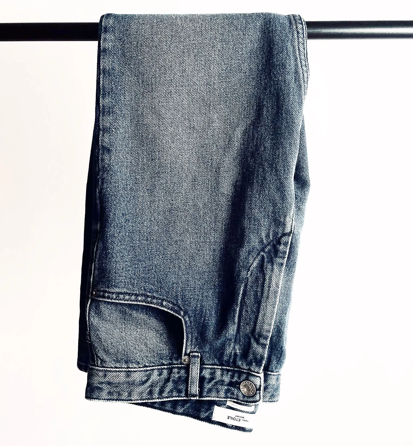 A pair of blue denim jeans folded over a black metal rod against a plain white background.