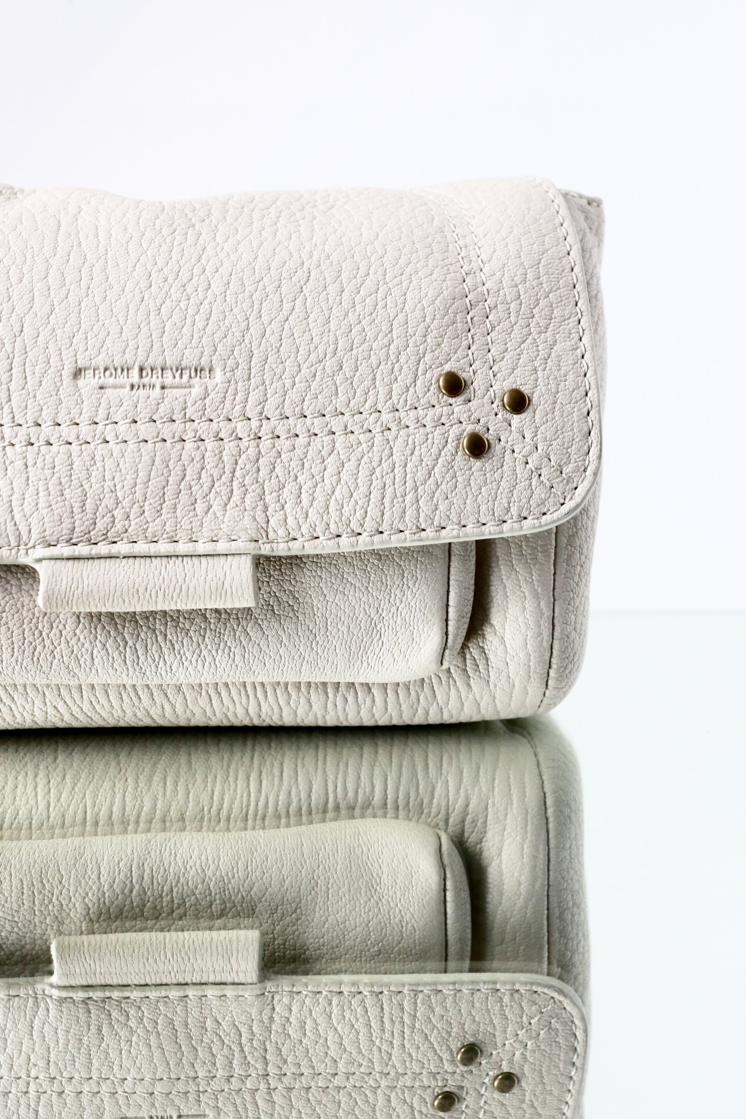 Close-up photo of a beige textured leather handbag on top of two matching textured leather cases, with a plain white background.