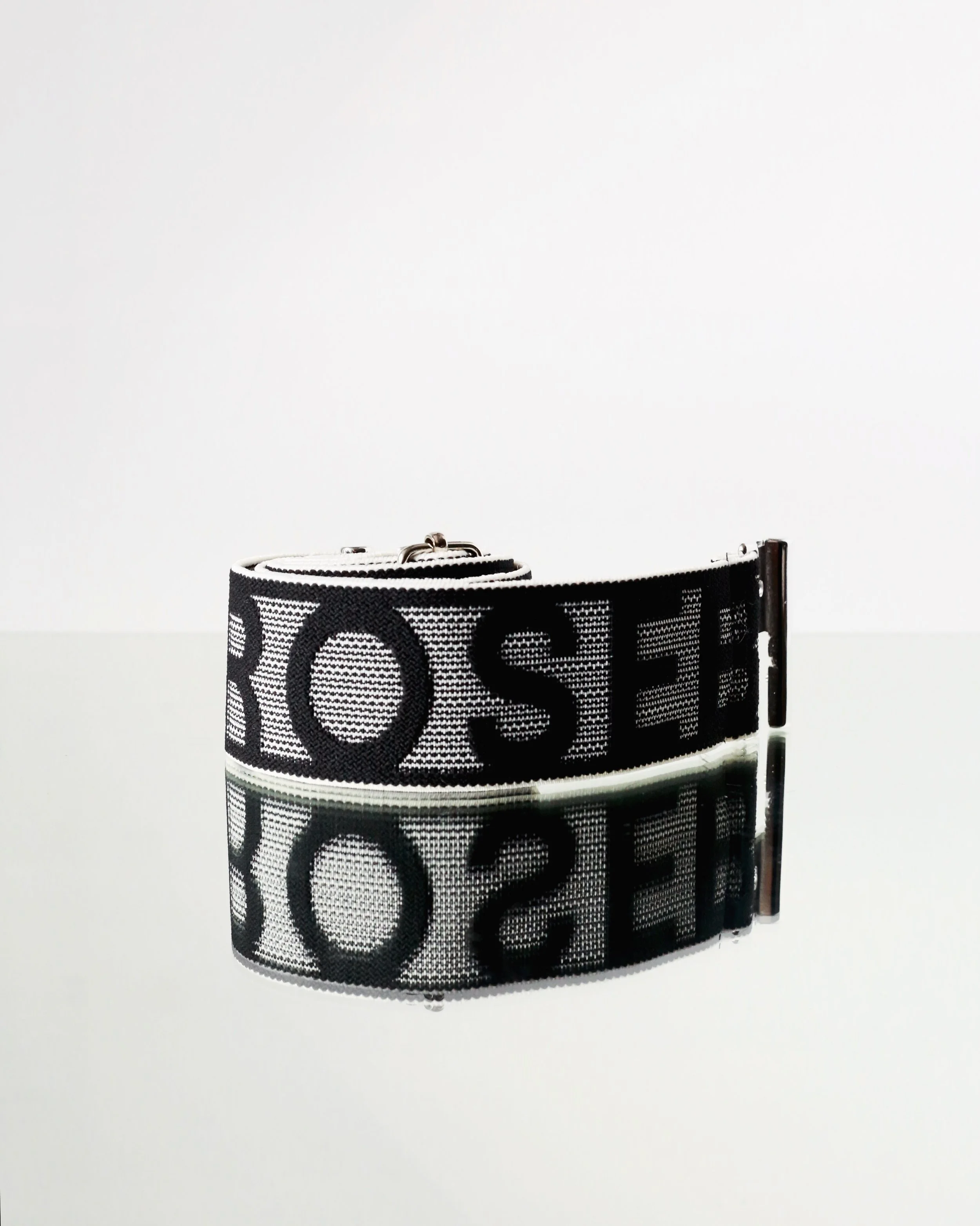 Black and white fabric belt with large letters and a metal clasp, reflected on a glossy surface.