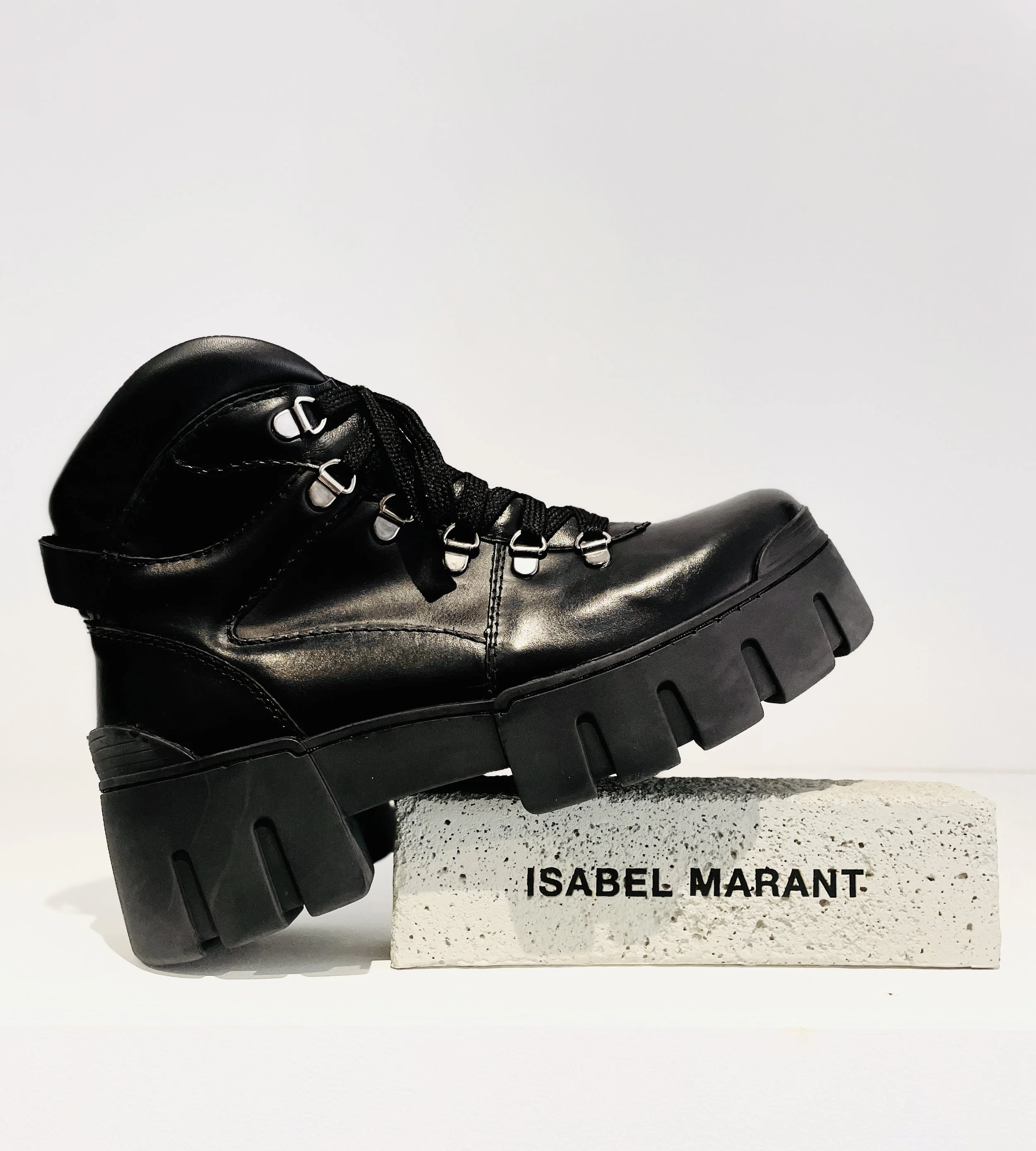 Black leather lace-up boot on a white textured block with 'ISABEL MARANT' printed on it, against a plain white background.