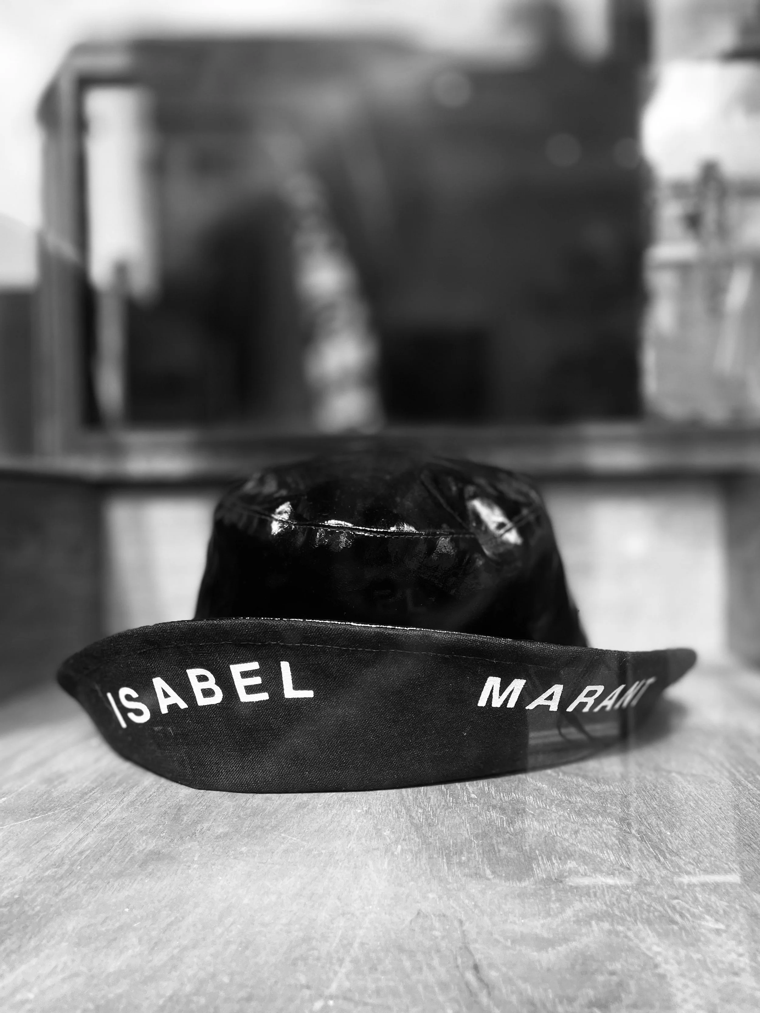 A black hat with a ribbon that has the name 'Isabel Marant' on it, resting on a wooden surface.