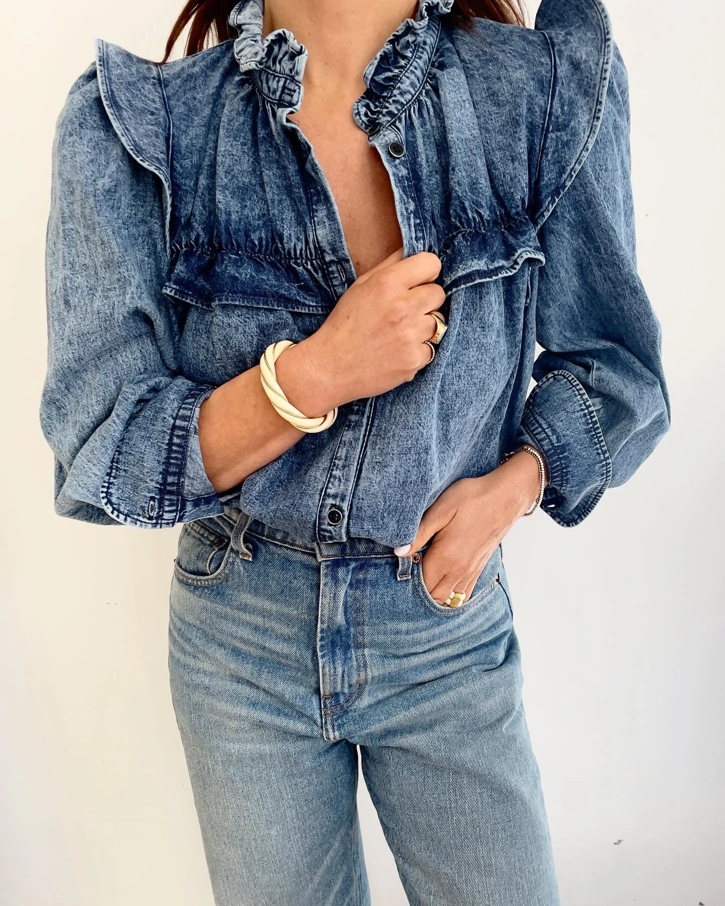 Person wearing a denim jacket with ruffled details on the shoulders and front, paired with matching denim jeans.
