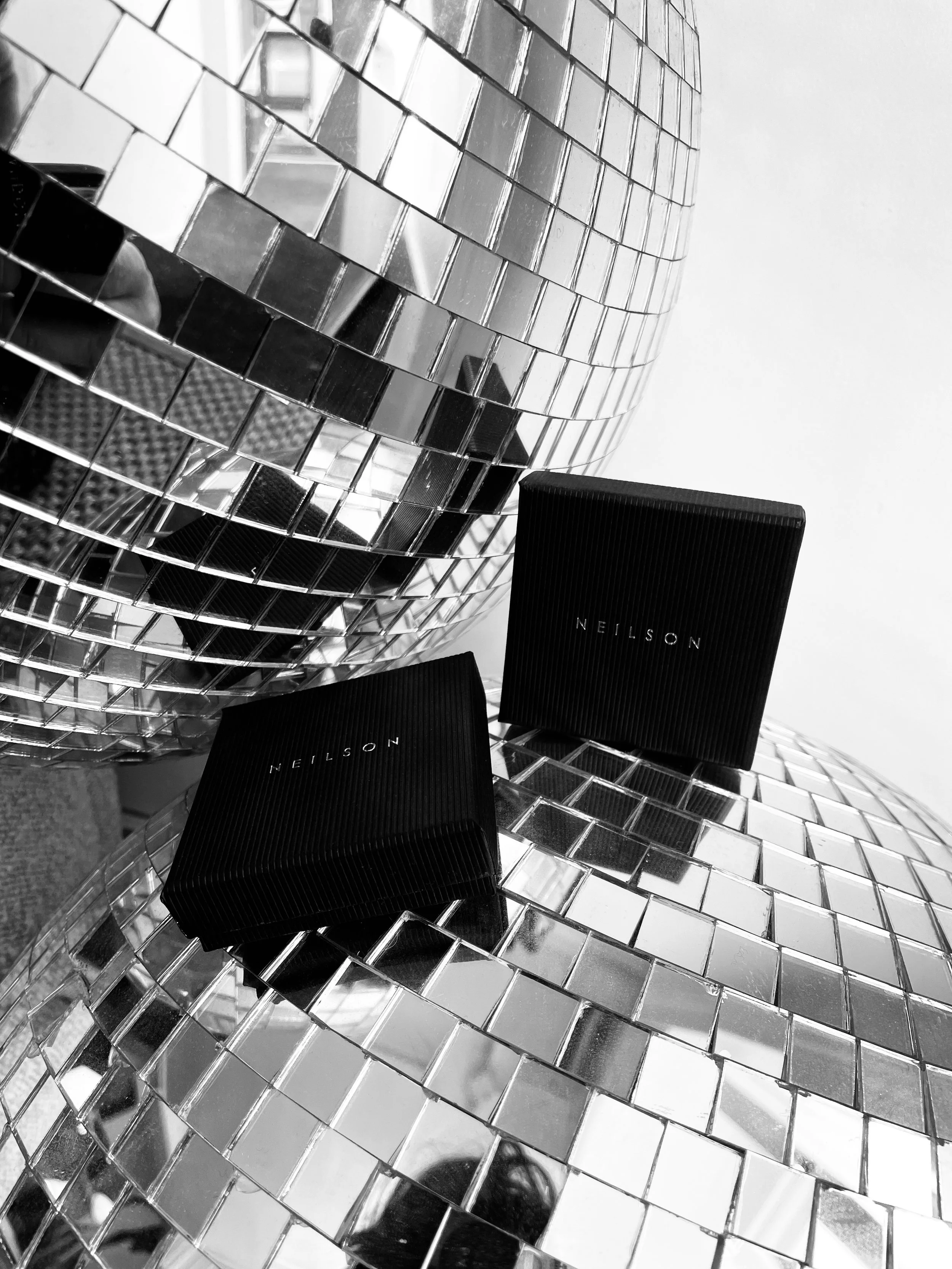 Two black boxes with the brand name 'Neilson' placed on a mirror mosaic sculpture composed of small square tiles.