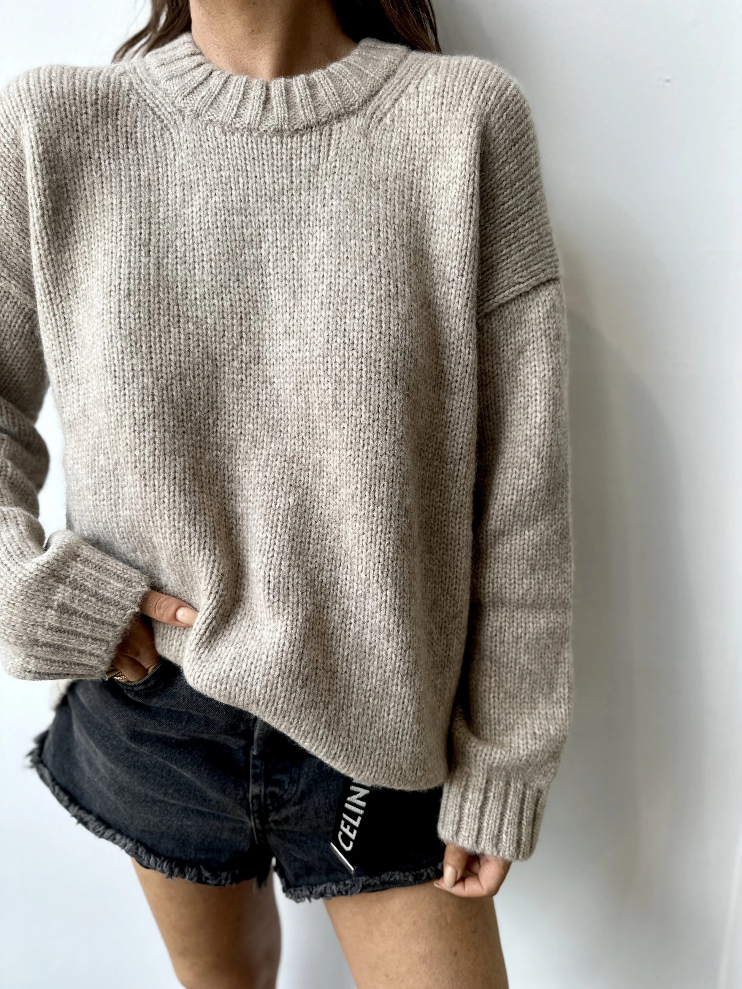 Person wearing a beige knit sweater and black denim shorts with frayed edges, against a white background.