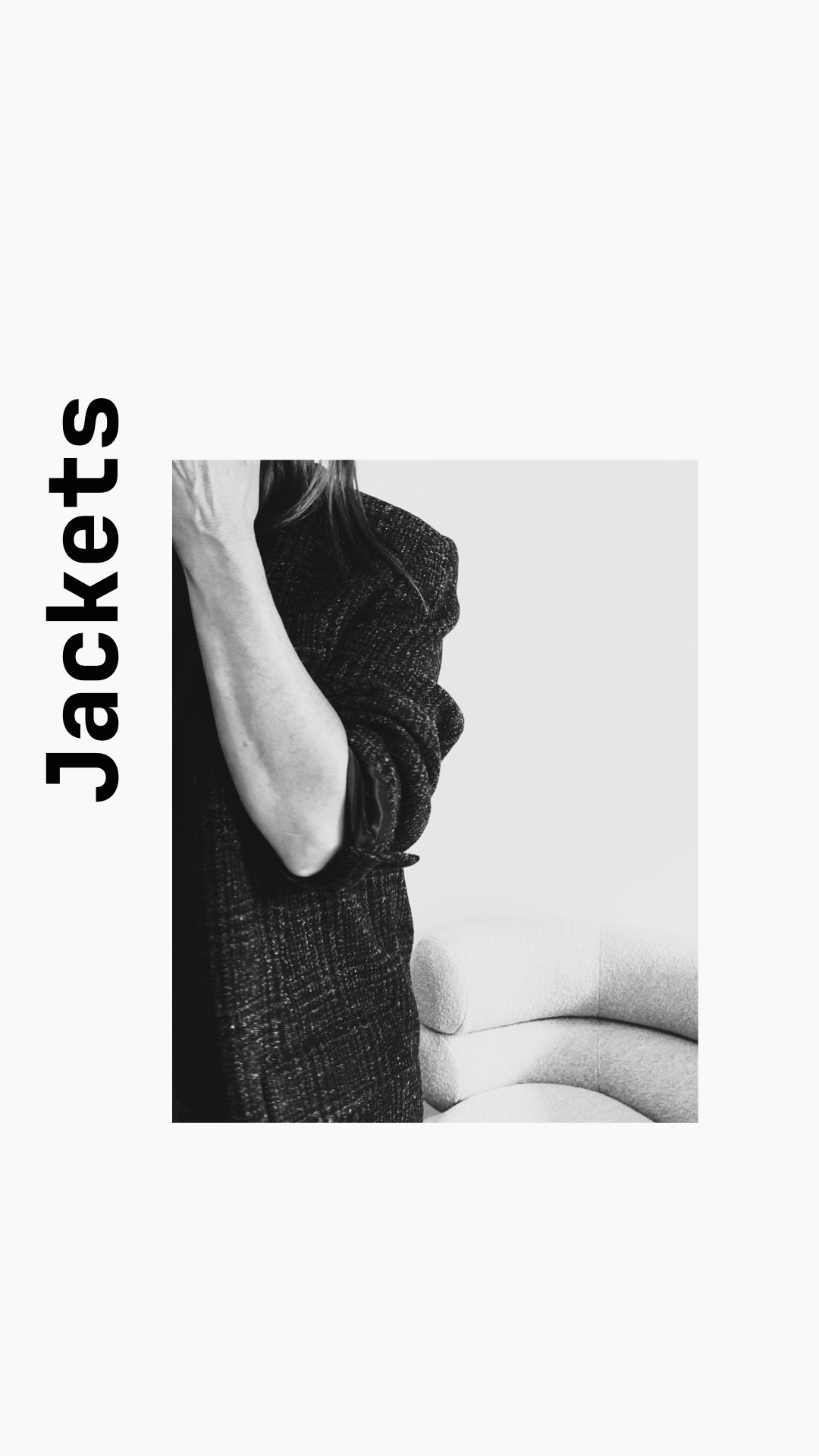 Black and white photo of a woman with long hair, wearing a dark textured sweater, standing next to a curved sofa. The image has text that says "Jackets" written vertically on the left side.