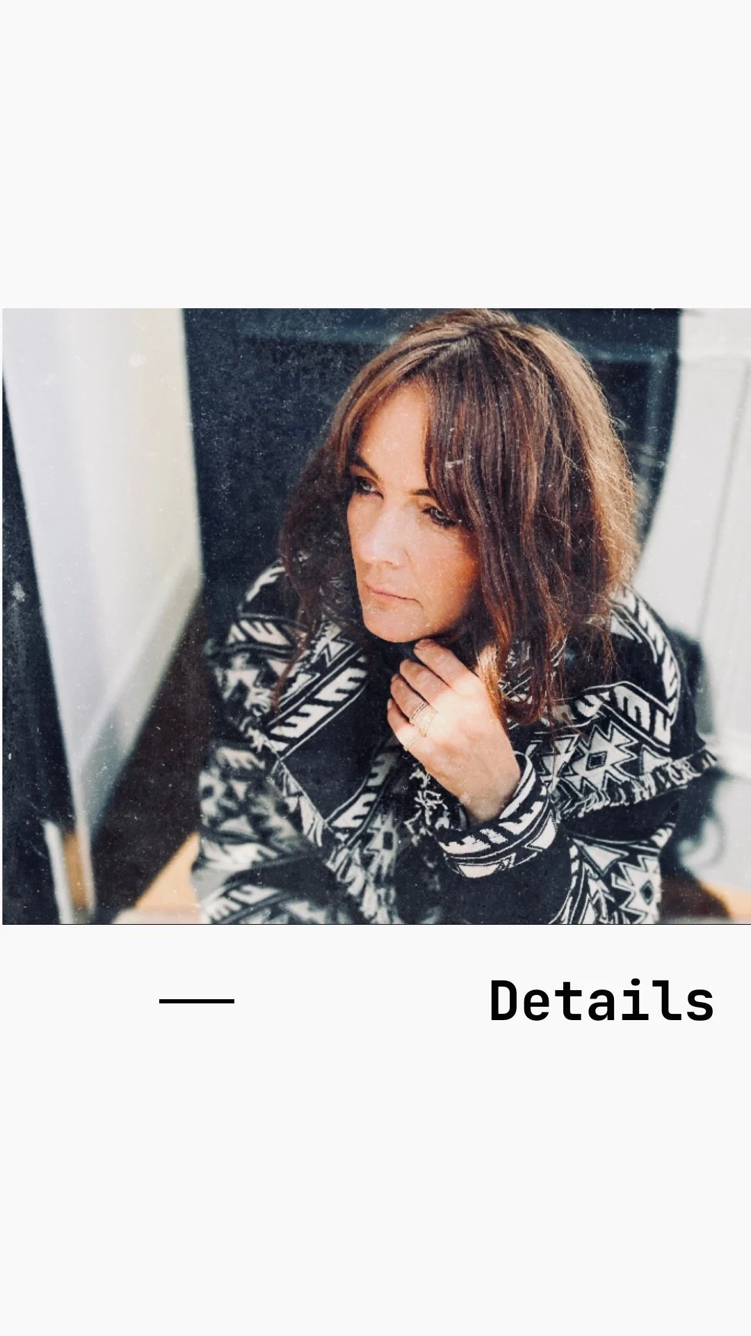 A woman with shoulder-length brown hair looking to the side, wearing a black and white patterned top, touching her chin with her hand, reflected in a mirror.