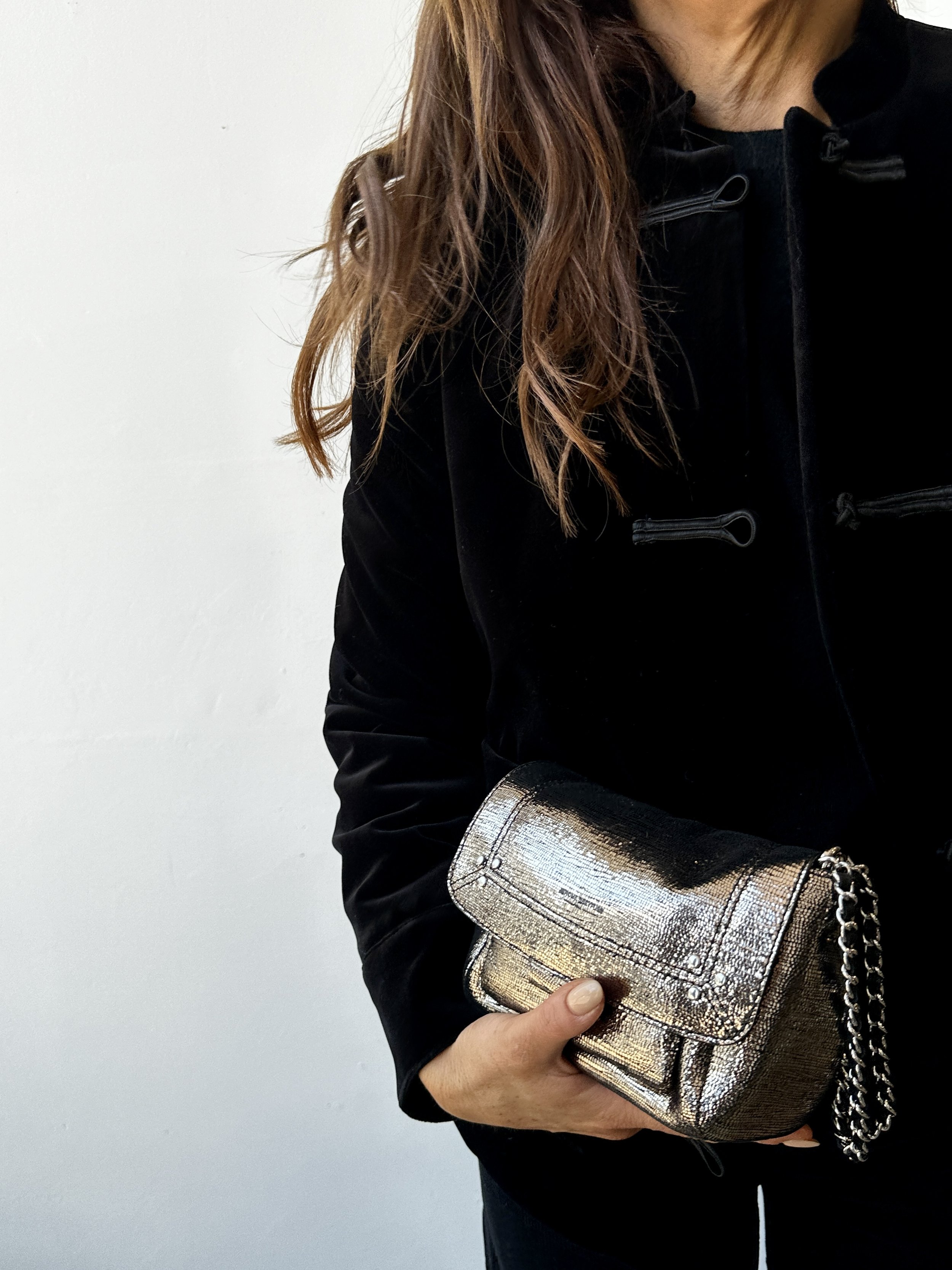 A woman wearing a black jacket holding a metallic gold clutch purse with a chain strap.