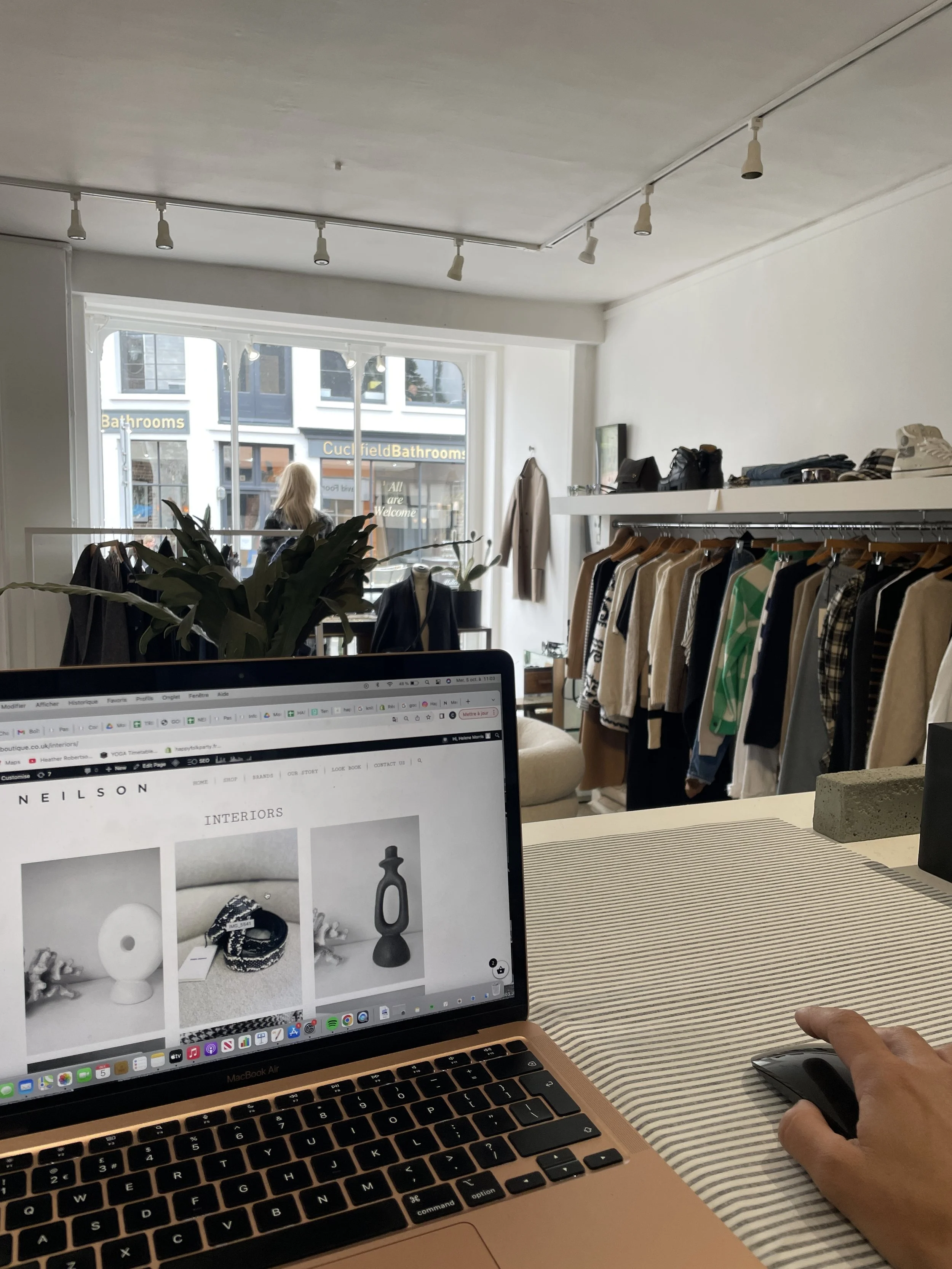 Indoor clothing boutique with clothing rack, shelves, and a person working on a laptop.