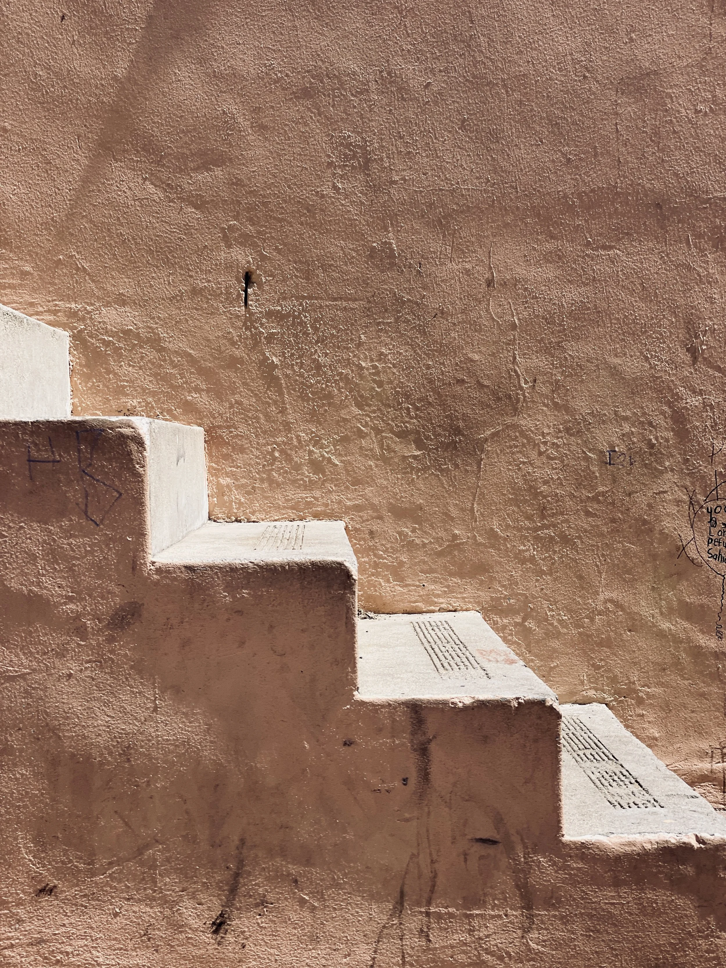 Concrete stairs against a textured beige wall with some graffiti and drawings.