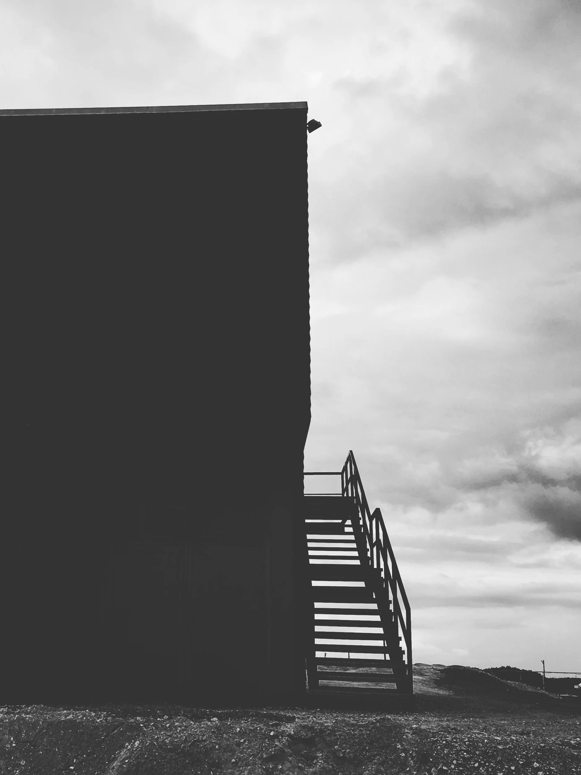 Black and white photo of a modern building with an external staircase on the right, against a cloudy sky.