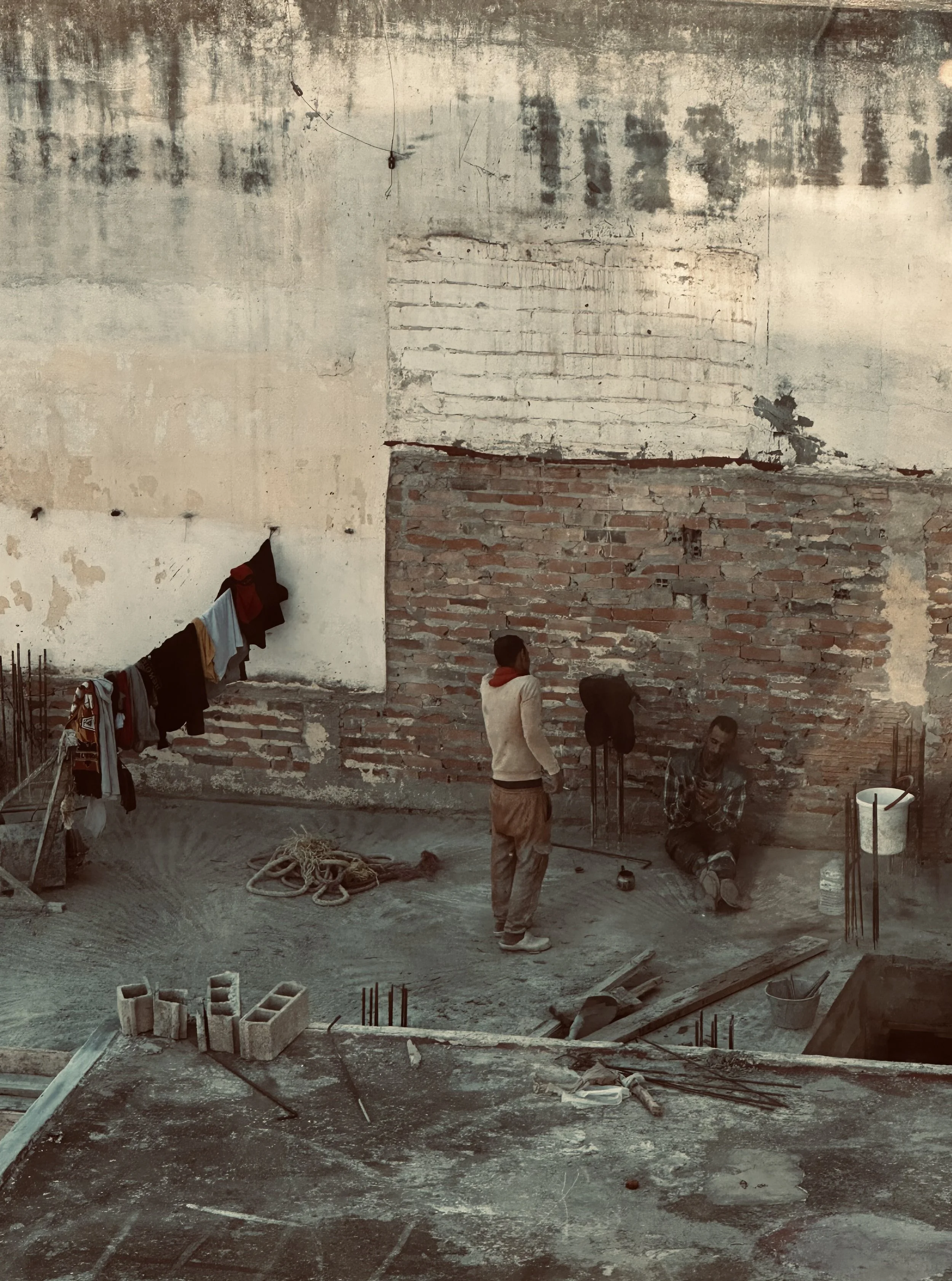 Construction workers on a building site with exposed brick and concrete walls, unfinished surfaces, and construction materials scattered around.