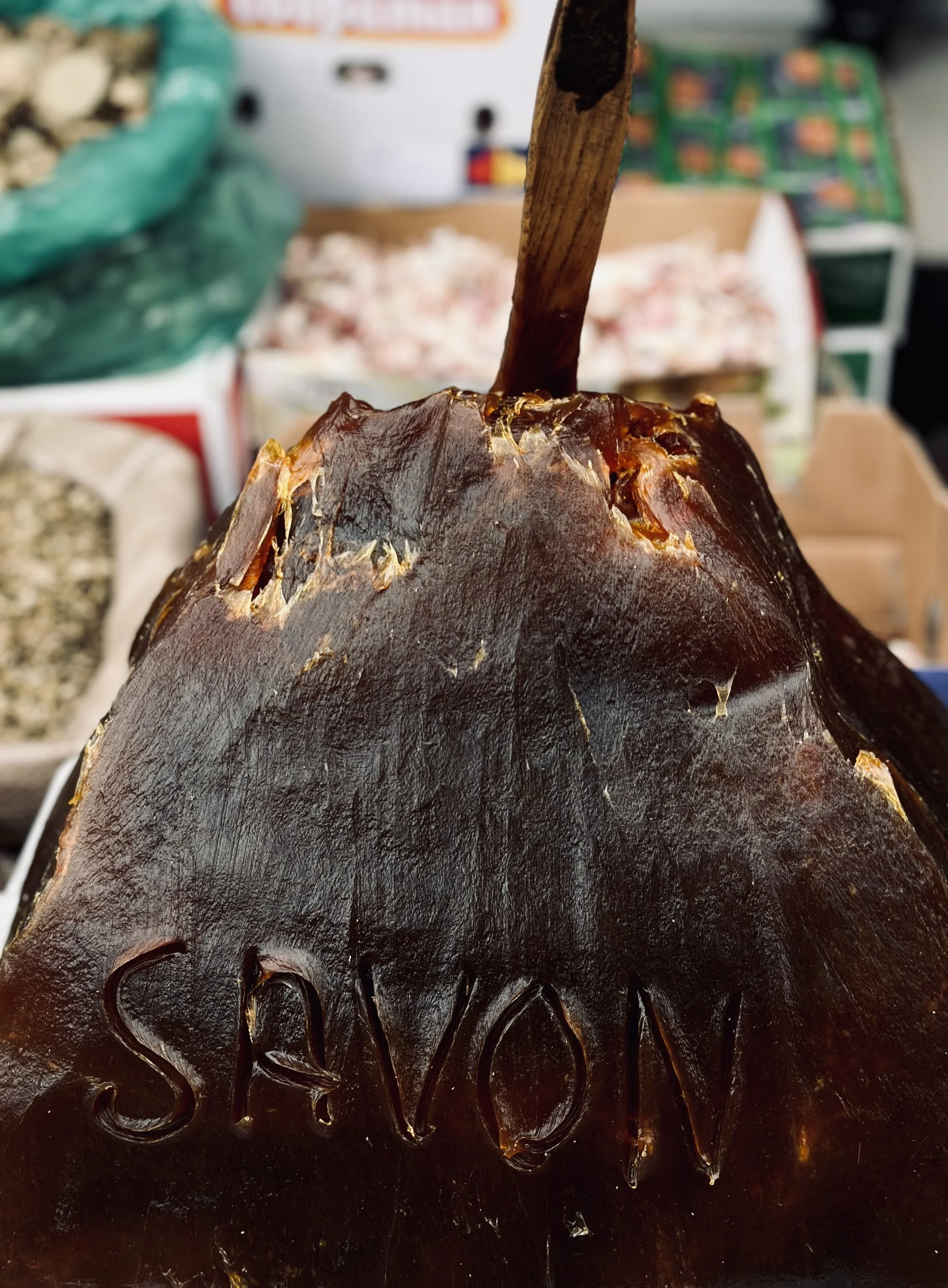 Close-up of a black pumpkin with the word "SAVON" carved into it, placed at a market or store display.