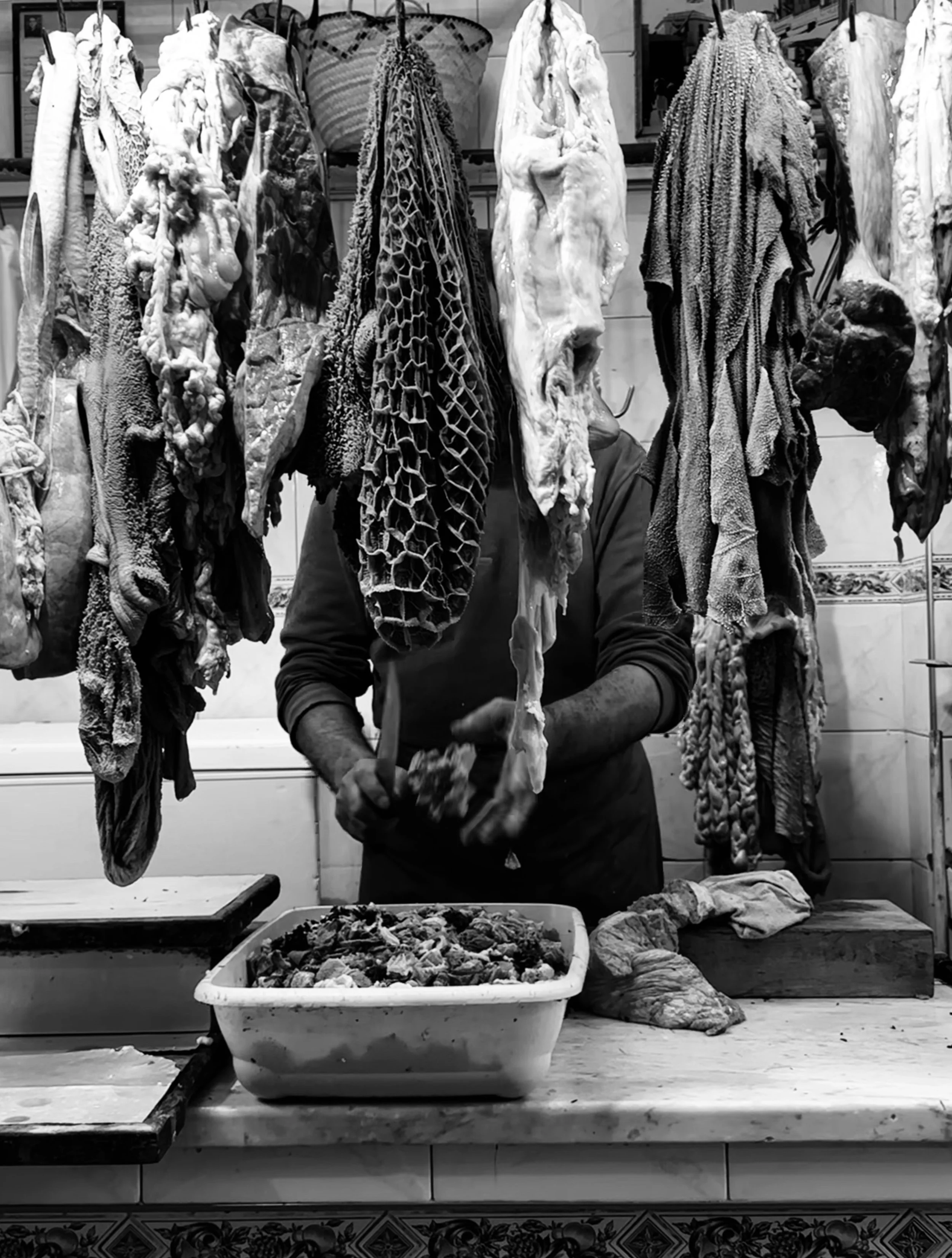 A butcher working with animal carcasses hanging in a shop, preparing meat on the counter.