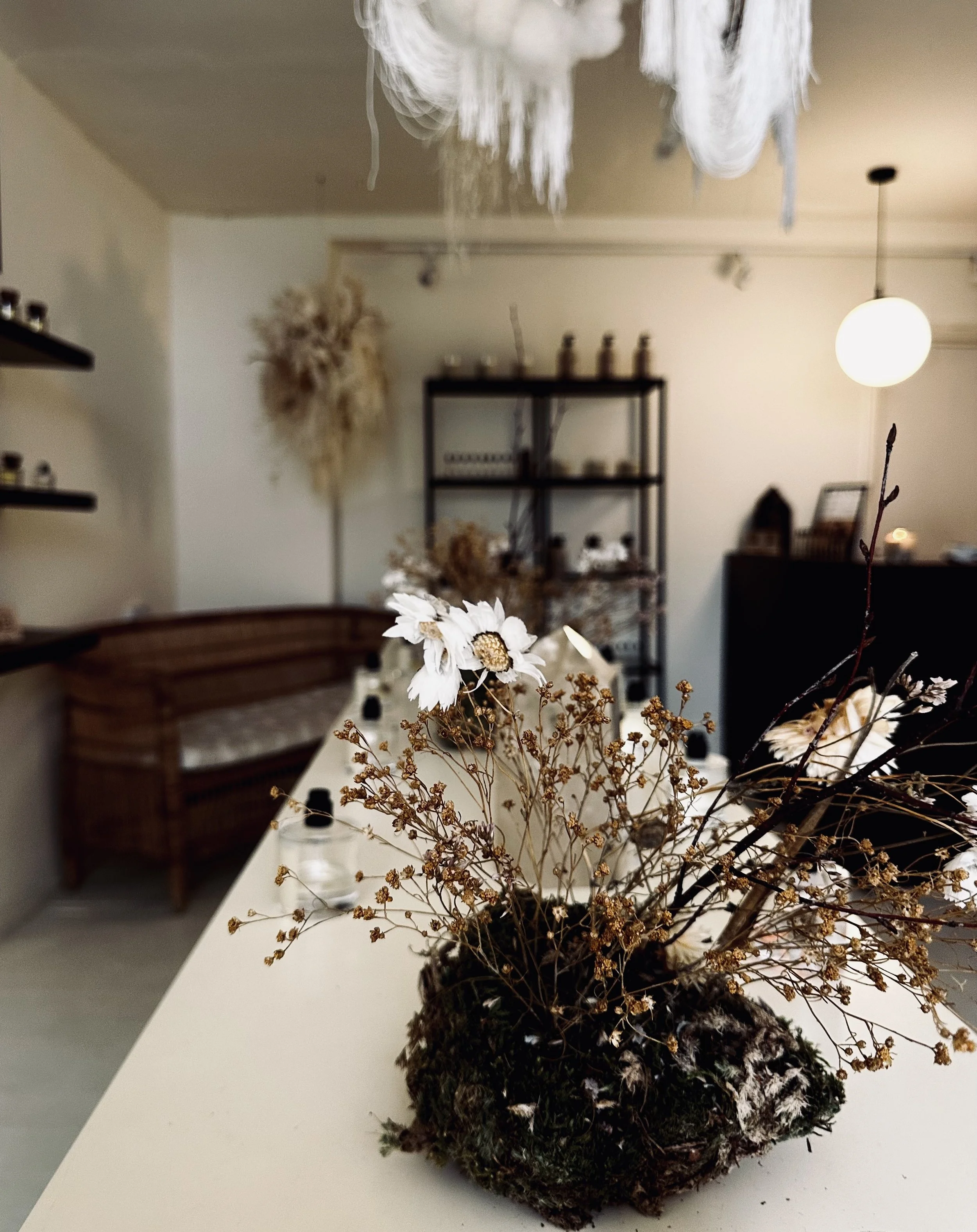 A close-up of a dried flower arrangement with white flowers and brown stems on a white surface in a cozy, well-lit room.