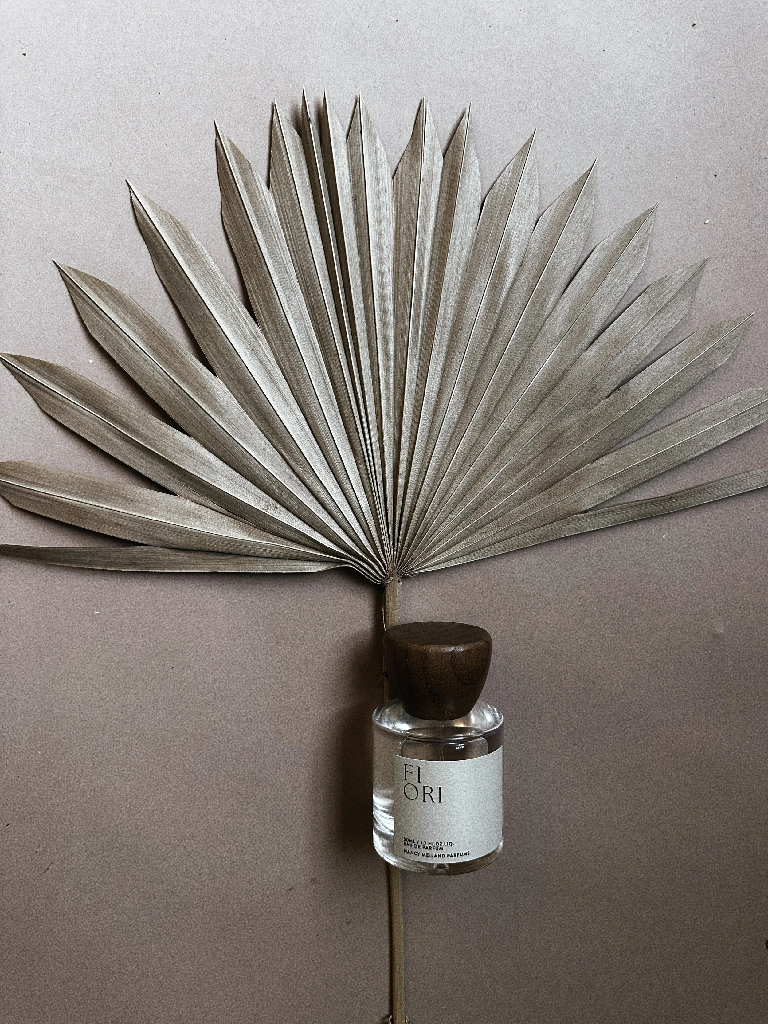 A dried, pale-colored palm leaf is inserted into a small perfume bottle, creating a decorative arrangement.