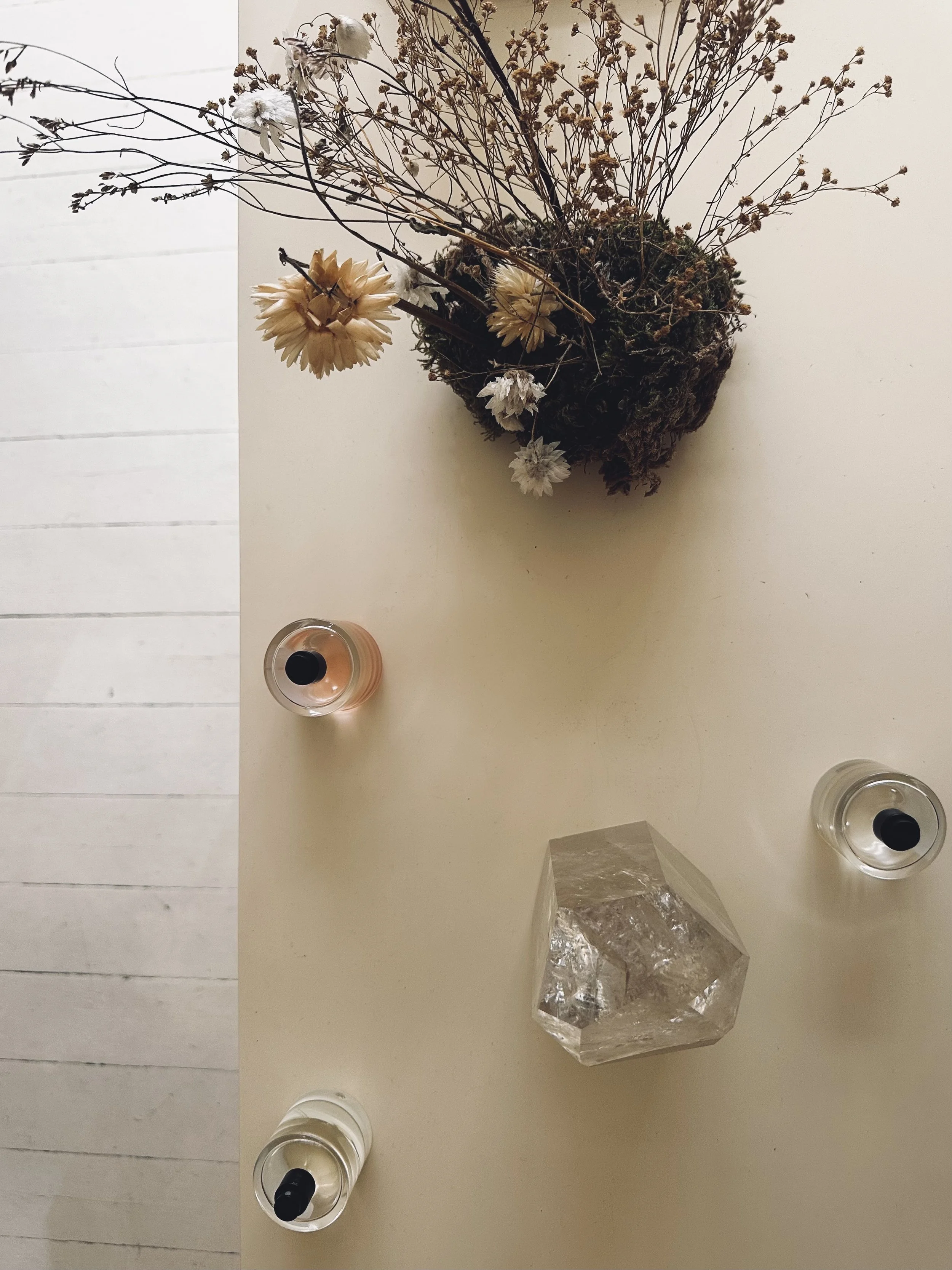 Top-down view of a table with dry flowers in a vase, two candles, and a decorative glass object.