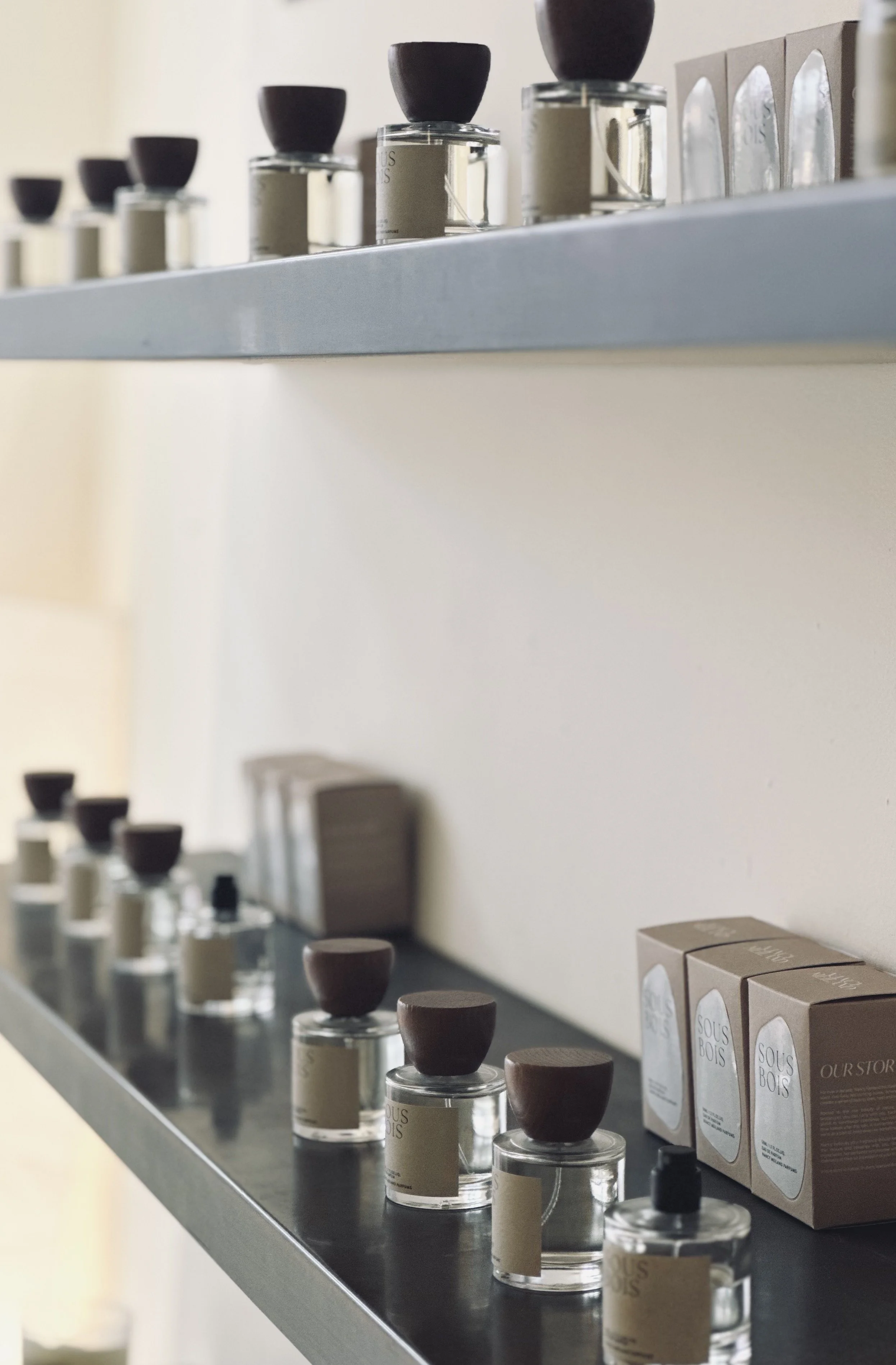 A display of small glass jars with black and wooden lids, lined up on black and white shelves, next to brown cardboard boxes labeled "Ours Bois."