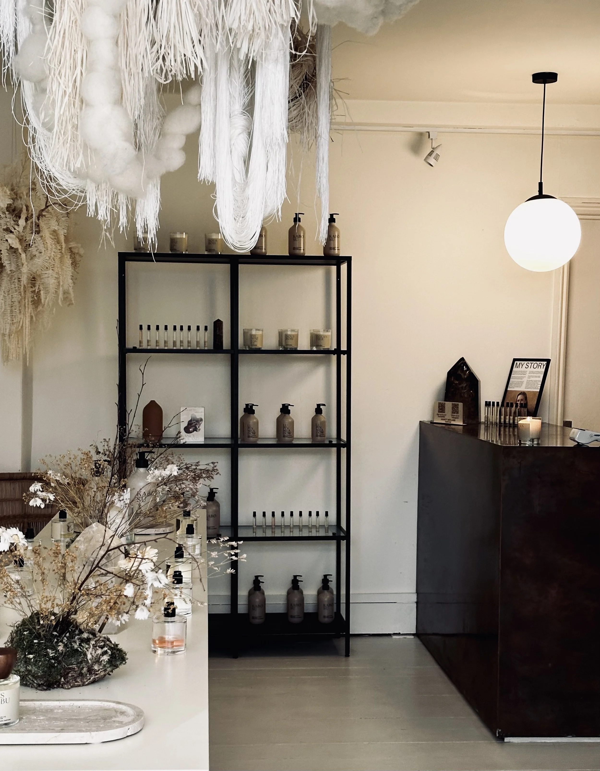 A minimalist interior with shelves of skincare products, dried flowers, and decorative hanging textiles.