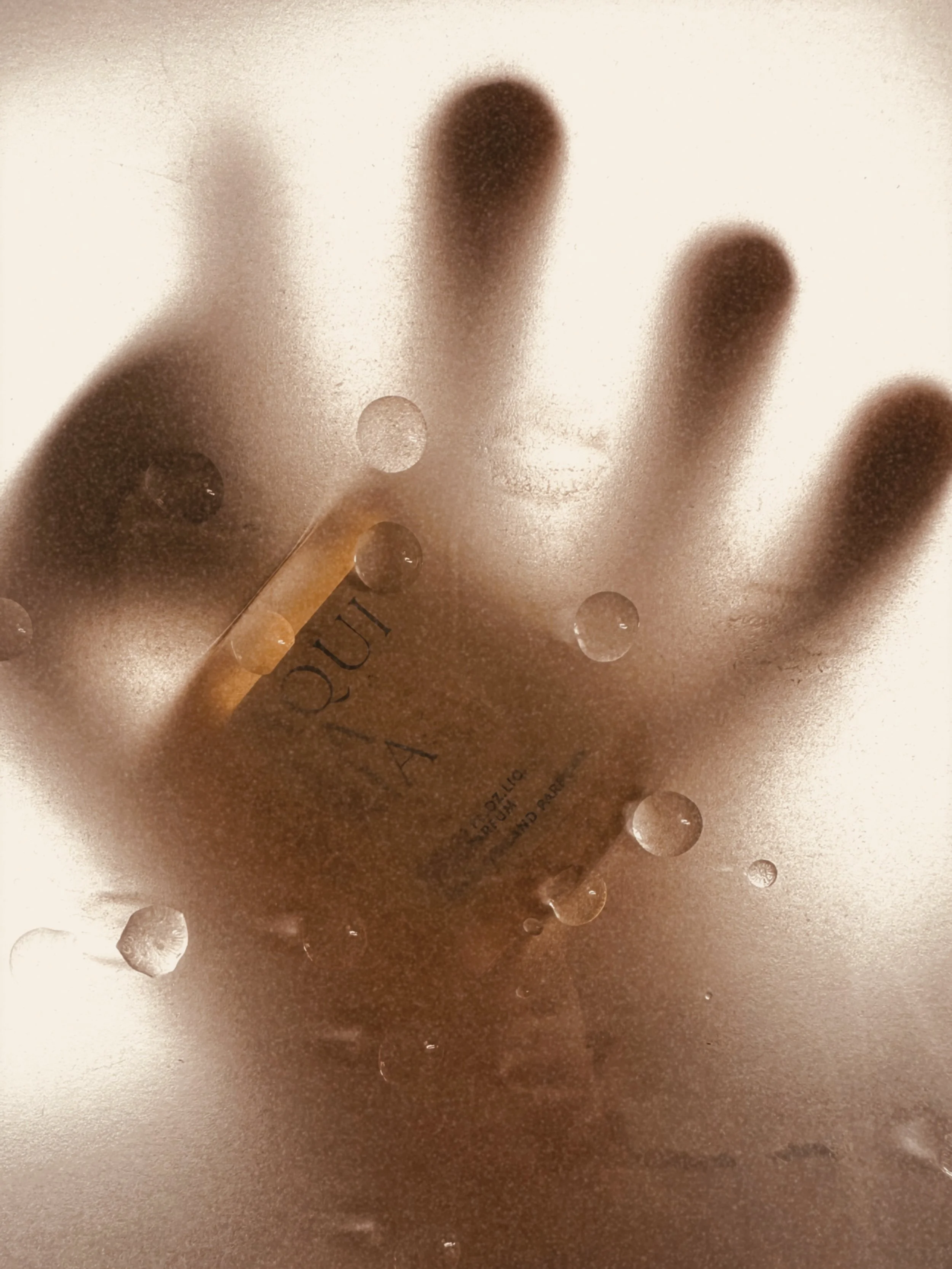 Frosted glass with a hand pressed against it, with a bottle of Vera Wang perfume behind the glass.