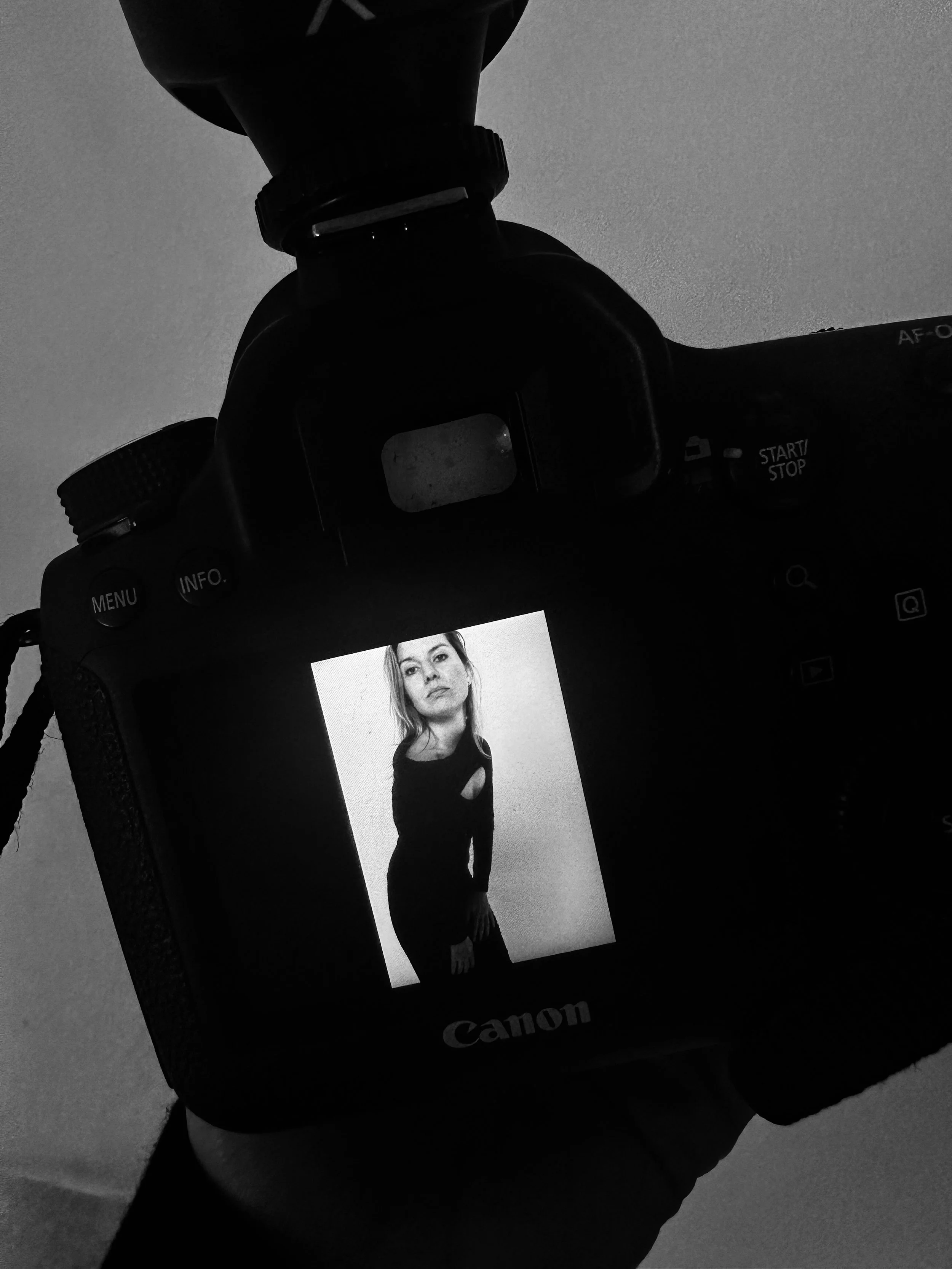 A digital camera displaying a black-and-white photograph of a woman with long hair, wearing a black dress with cut-outs, standing against a plain background.