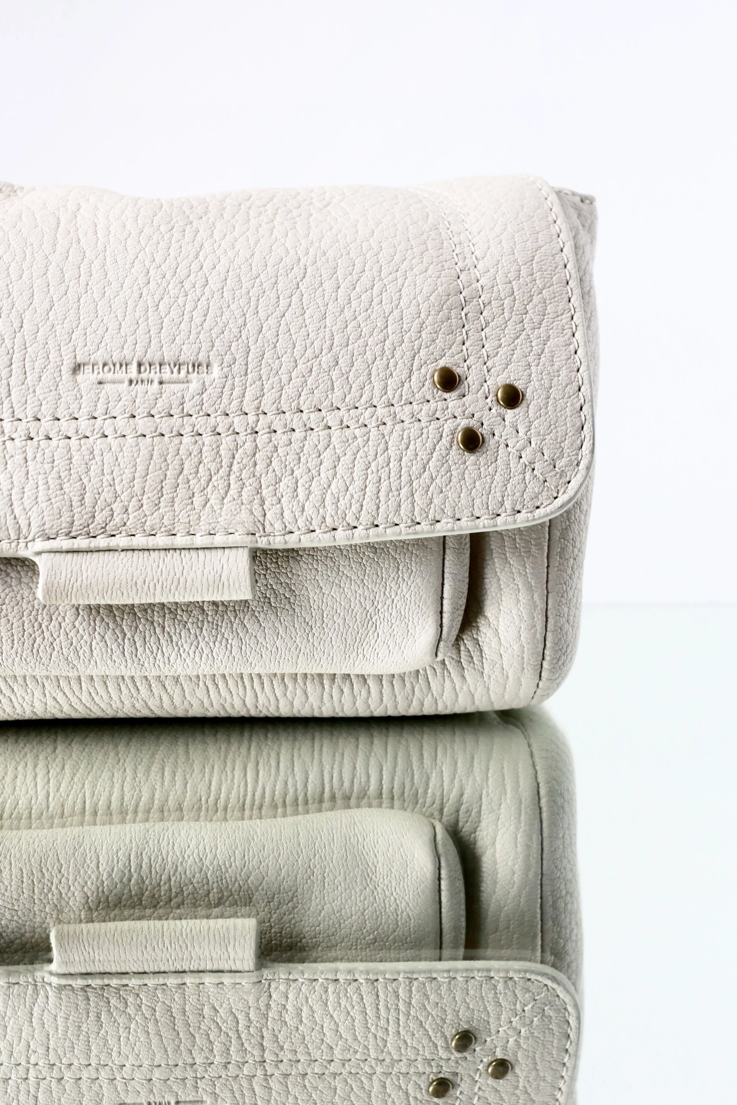 Close-up photo of stacked off-white textured leather bags with minimal metallic accents.
