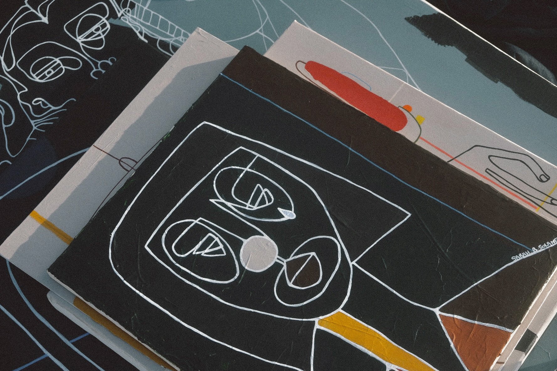 Stack of graphic design books with abstract line art covers, featuring a face outlined in white and black, with various color accents, on a table.