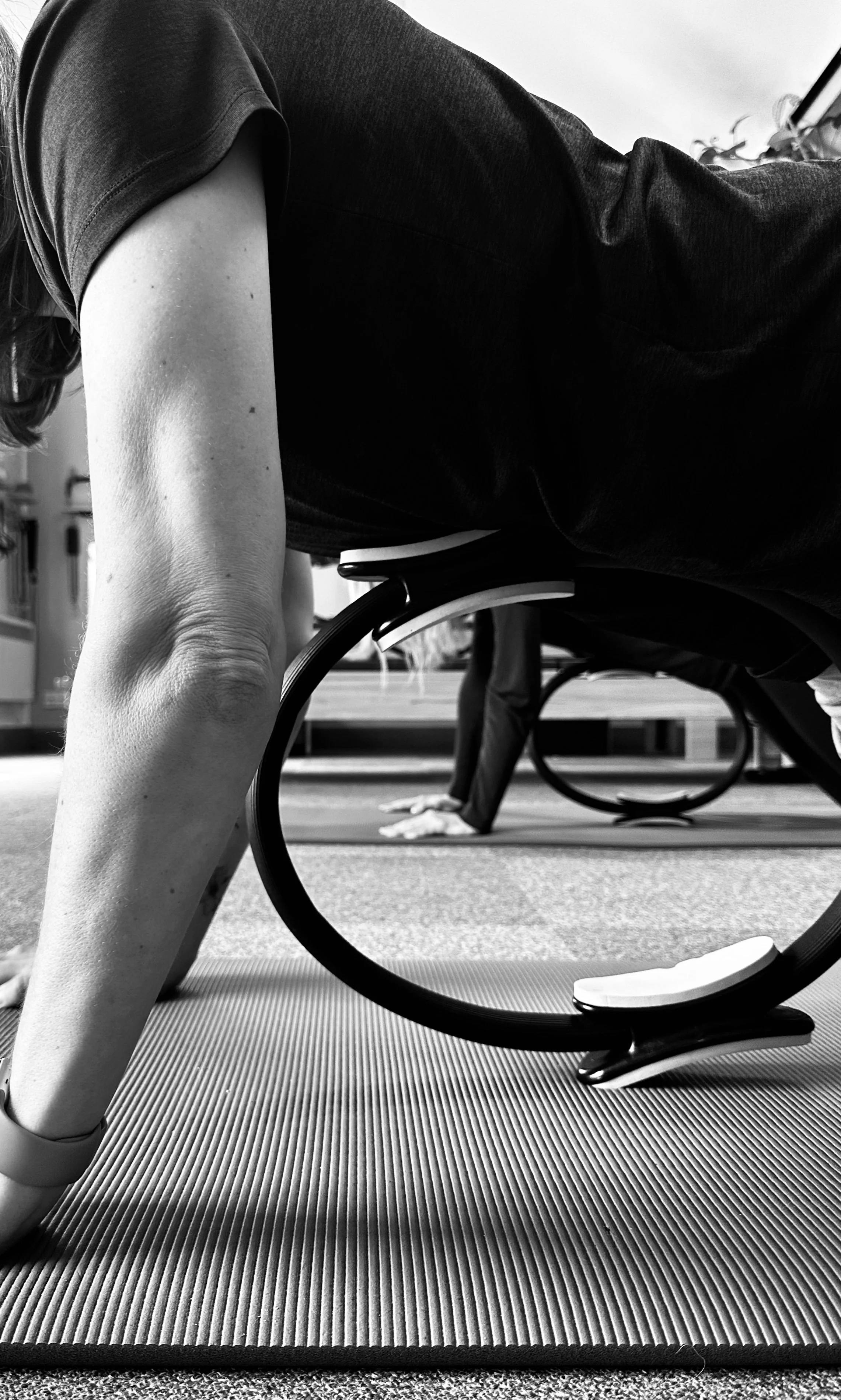 People practicing yoga in a studio, doing plank pose on mats, with a focus on the arm and elbow of one person.